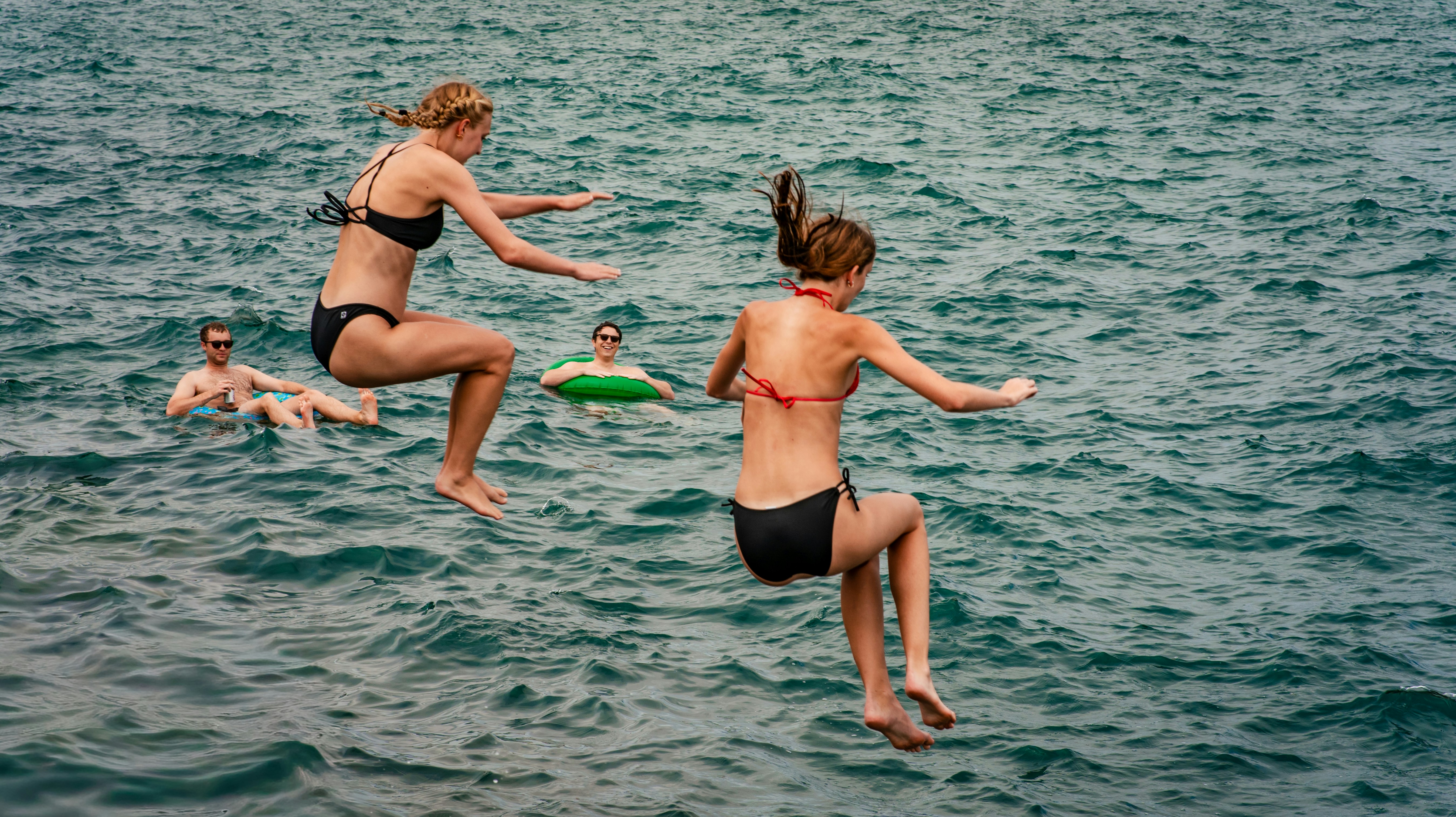 Two women jumping into the sea while two people float nearby