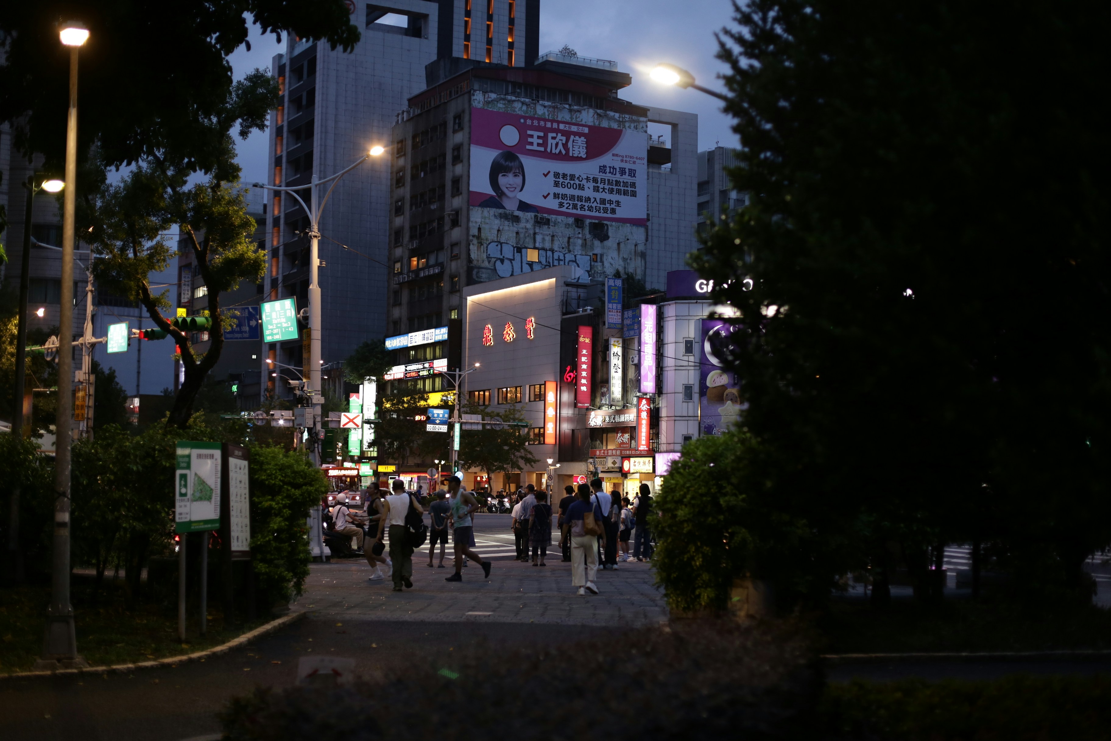 People walking on a sidewalk near illuminated city buildings at night