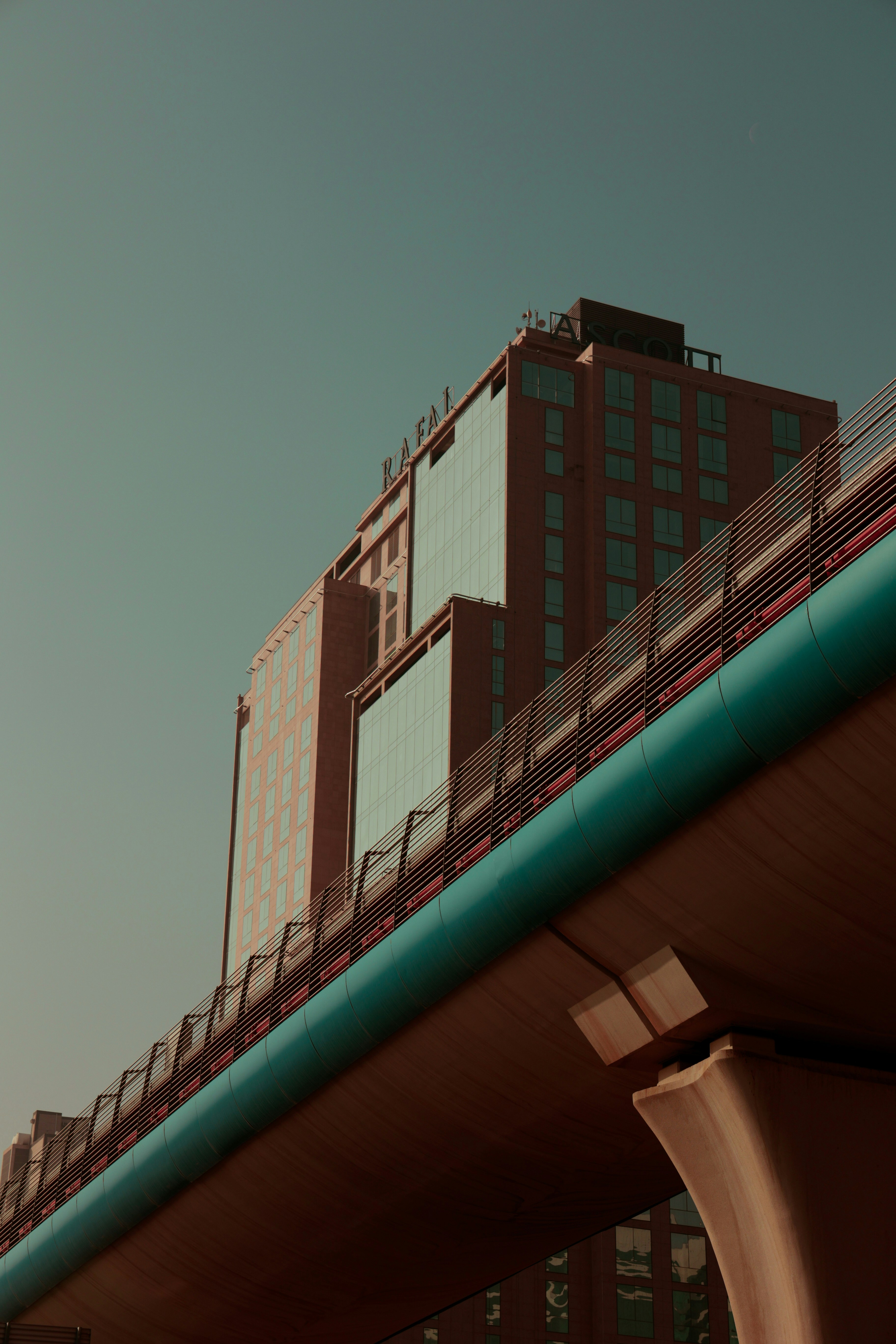 A modern glass and brick building behind an elevated teal pedestrian bridge