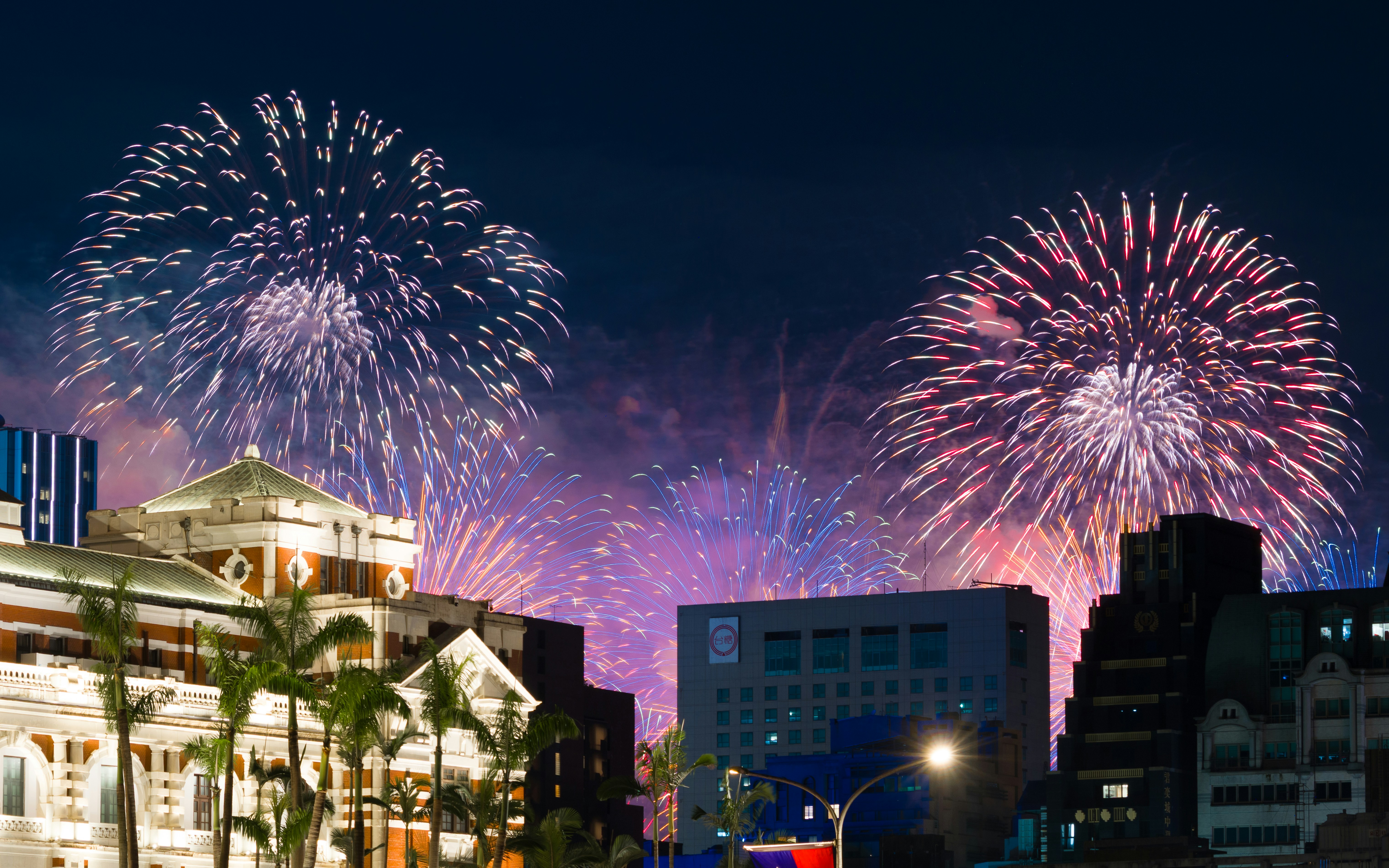 Colorful fireworks exploding over a city skyline with palm trees at night