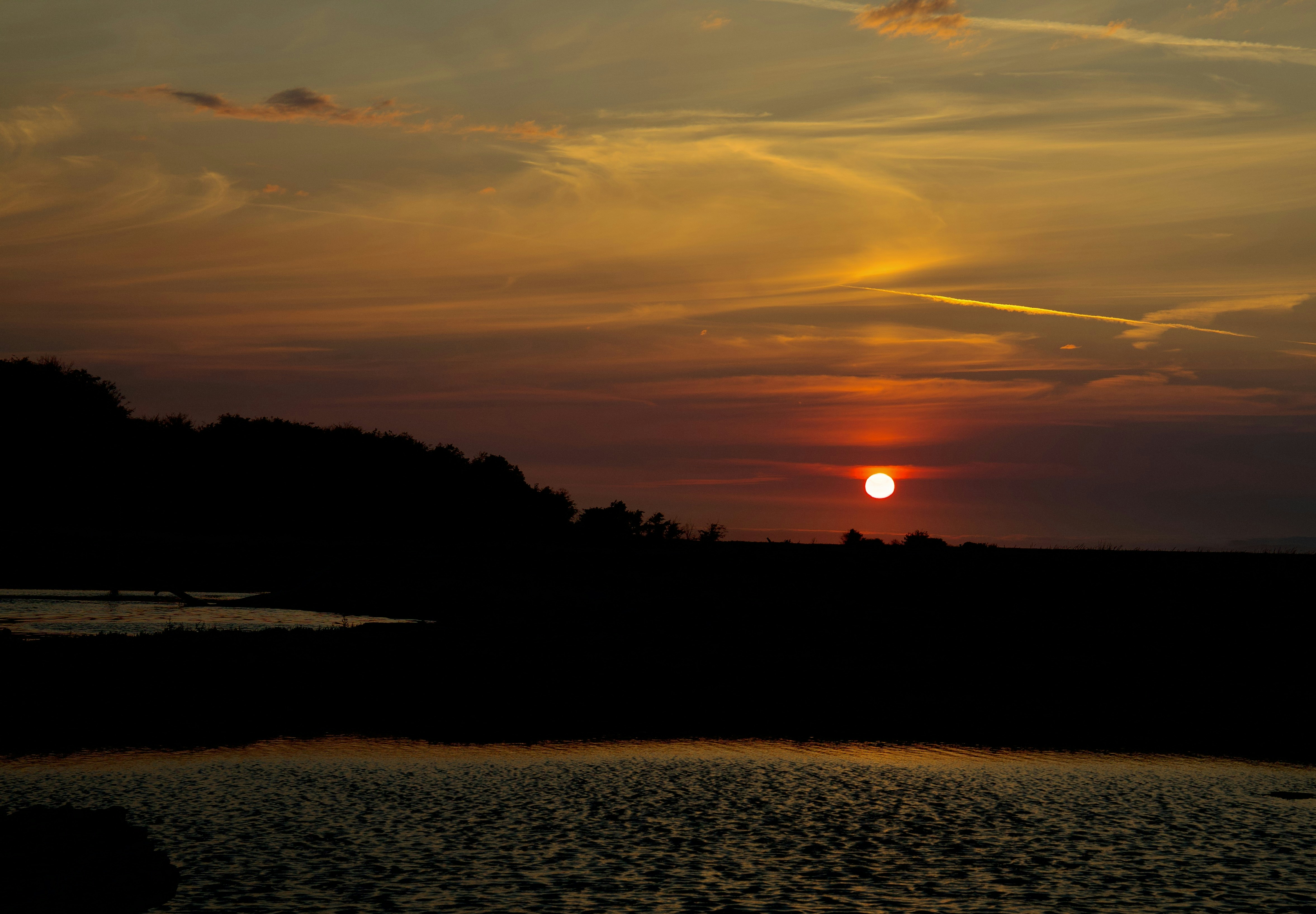 Low sun in a warm orange sky above a dark silhouette of land