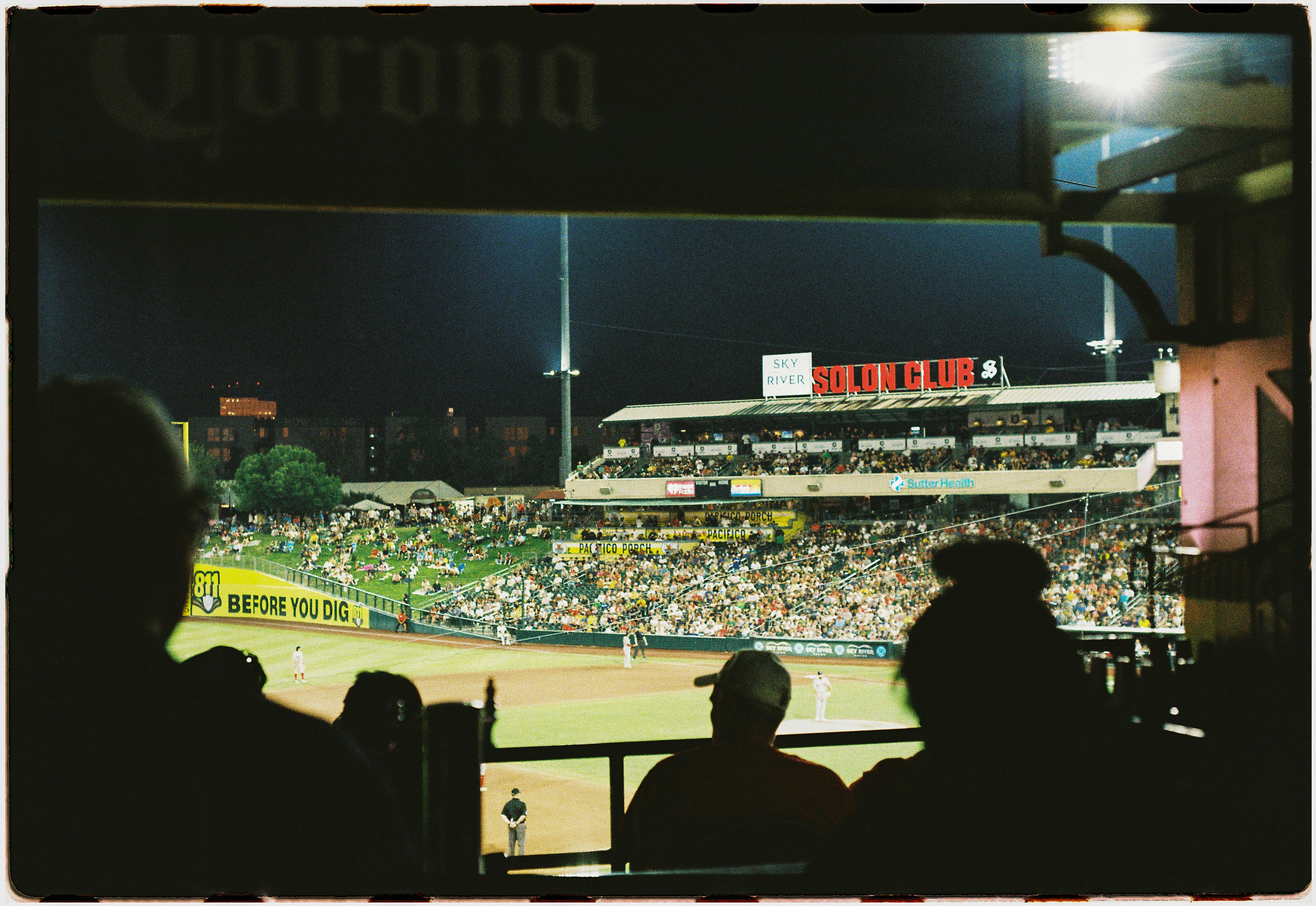 Espectadores em silhueta assistindo a um jogo de beisebol noturno de uma suíte no estádio
