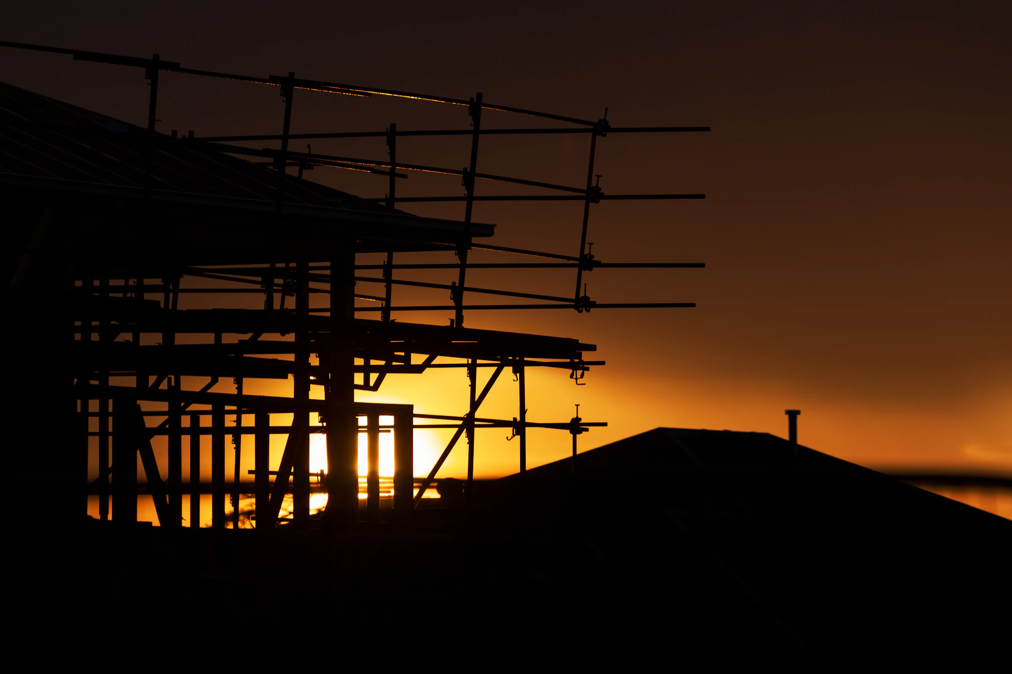 Charpente de maison en construction à contre-jour, au lever du soleil
