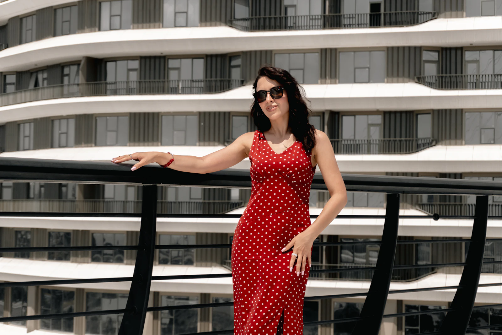 Woman in a red polka dot fitted midi dress leaning on a railing