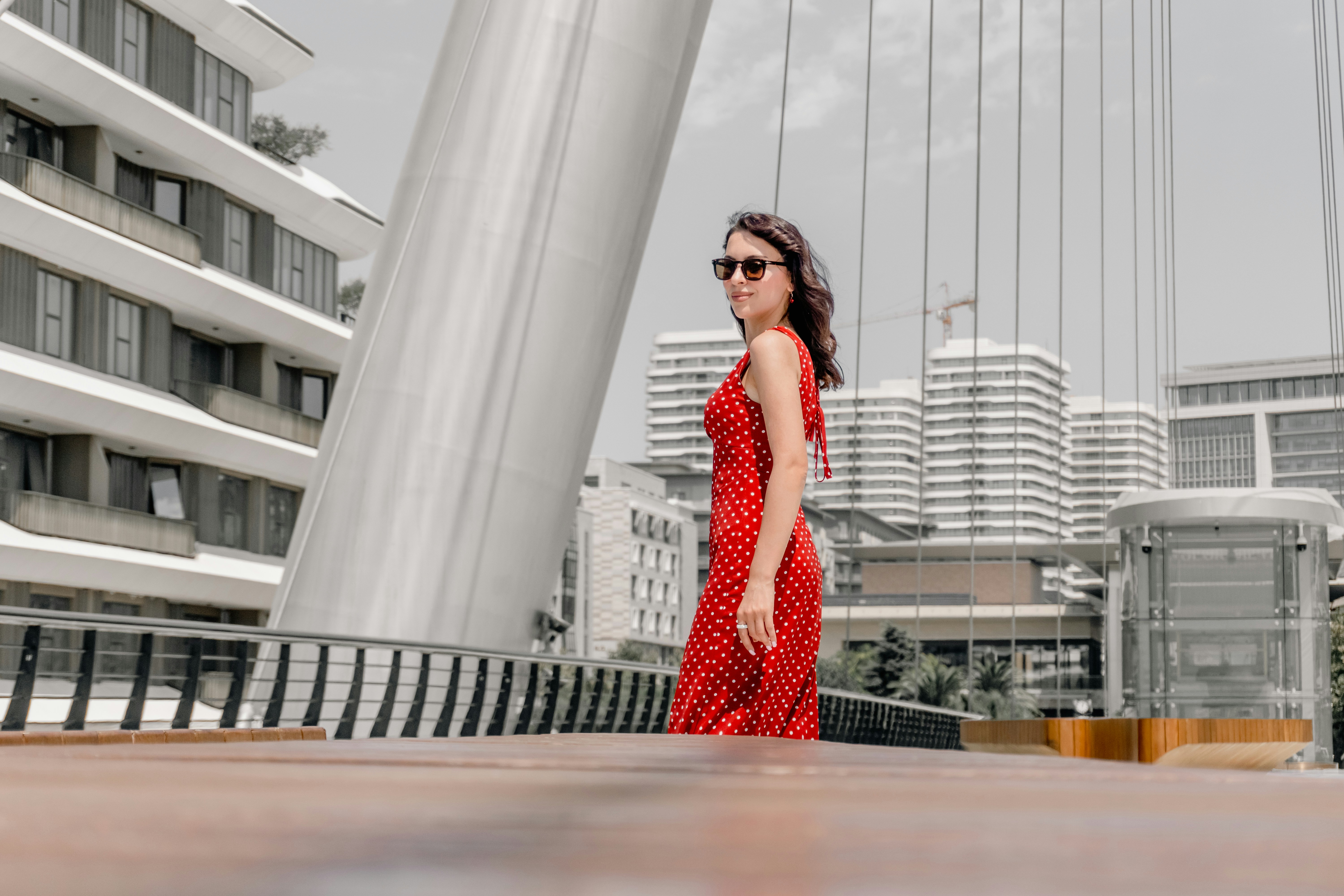 Woman in a red polka dot dress and sunglasses on a modern bridge