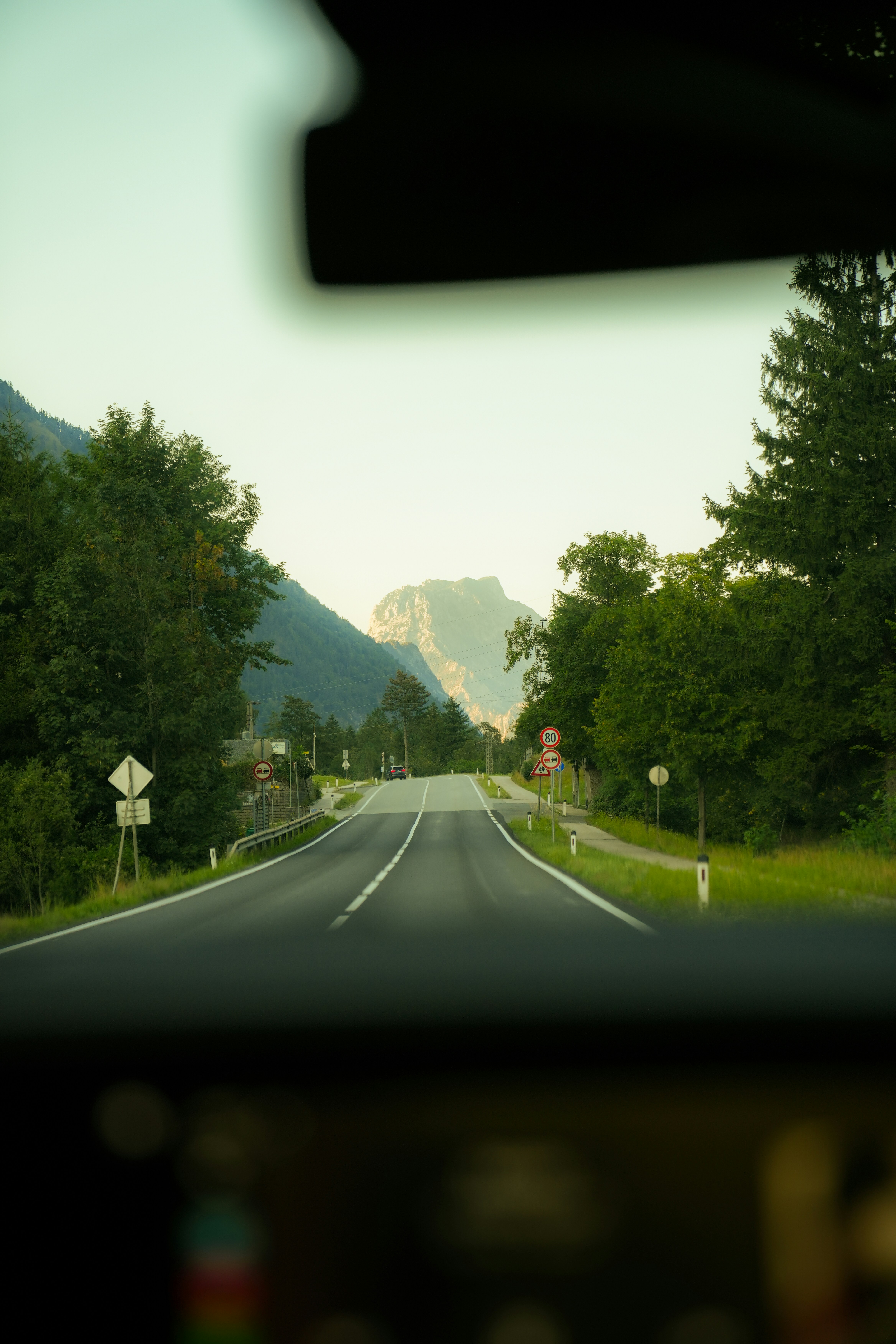 A paved road leading toward distant mountains through a tree-lined landscape