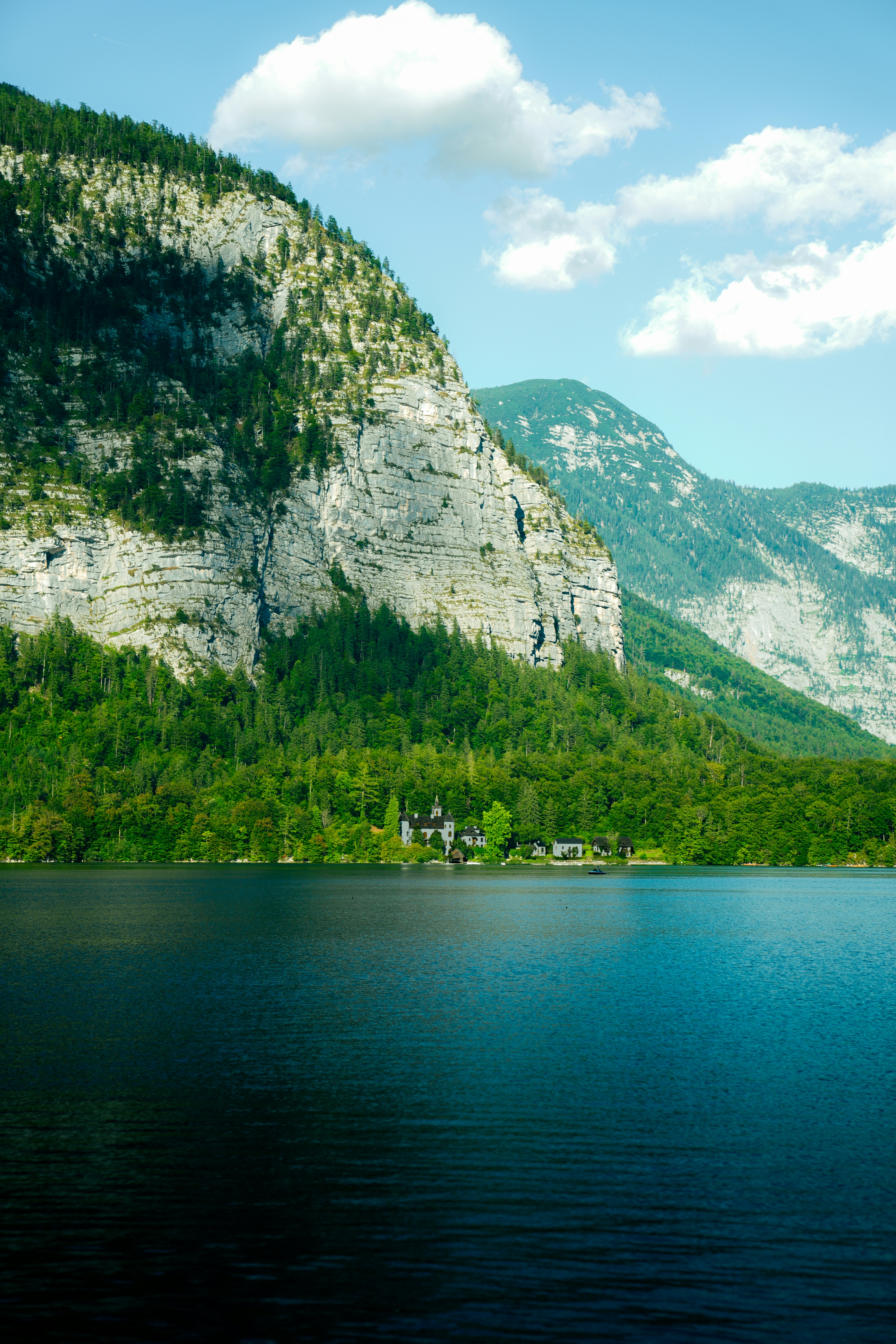 A small cluster of buildings on the shore of a lake beneath a steep mountain