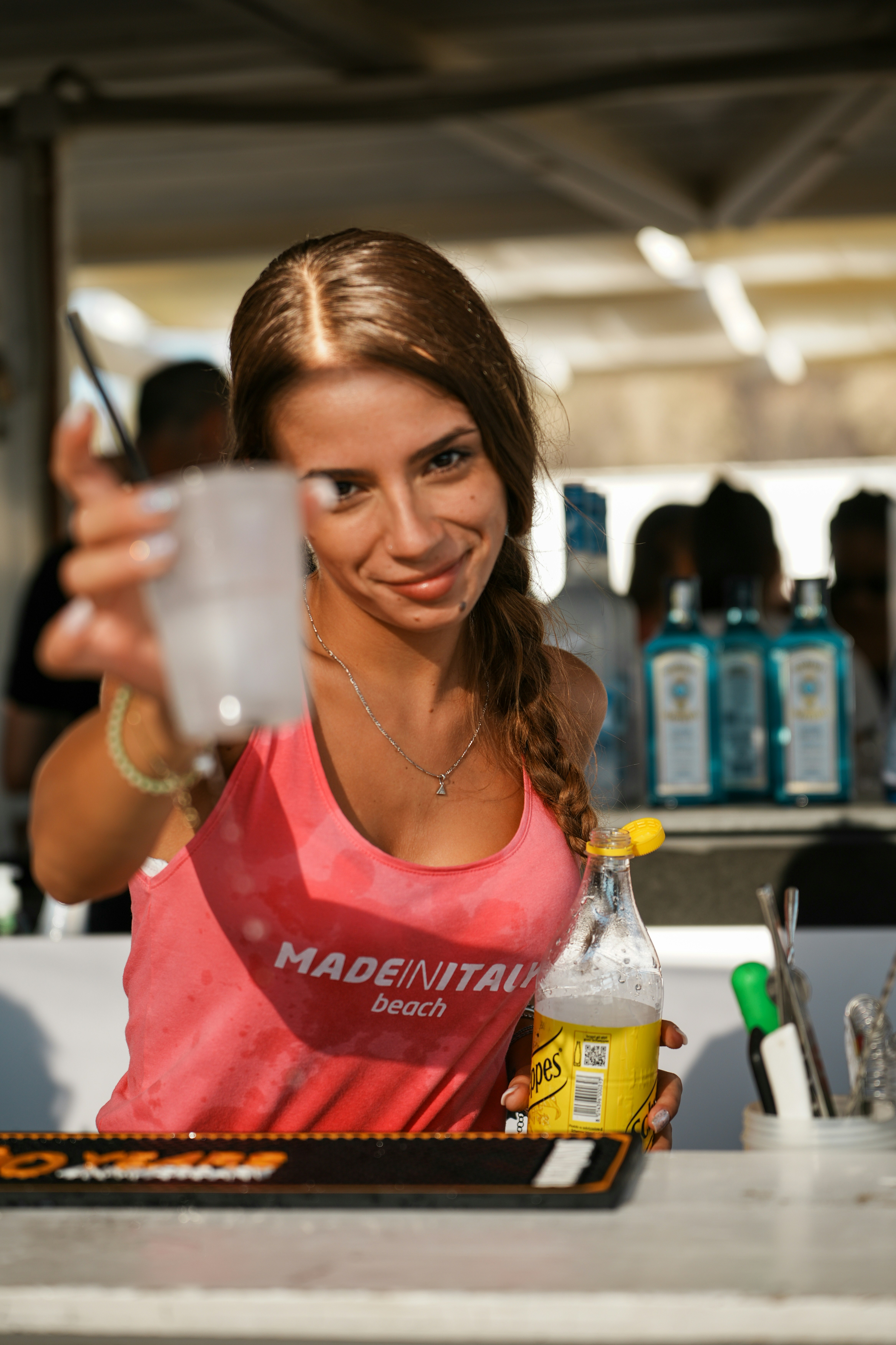 A woman in a pink tank top holding a drink at a bar