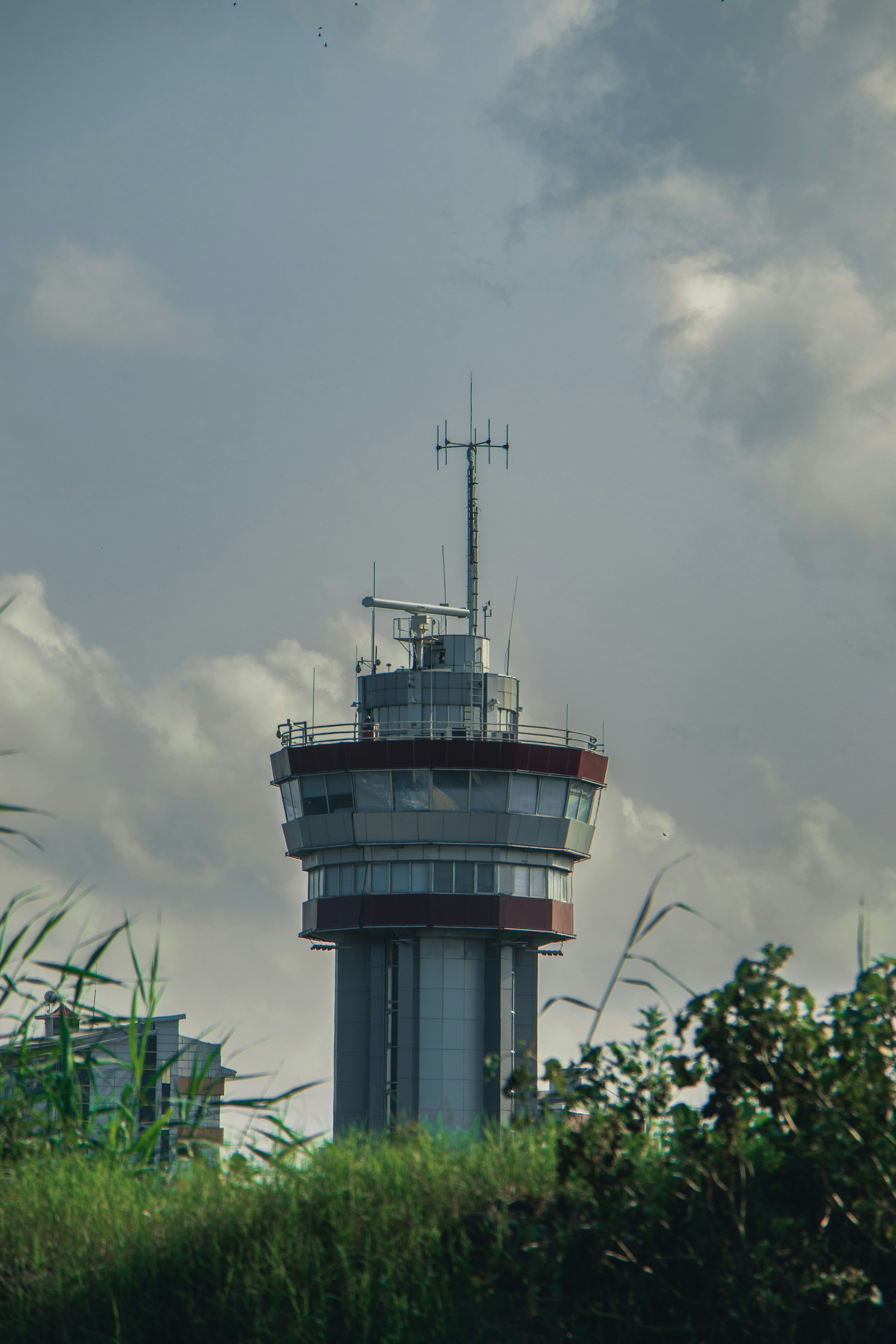 Una torre de control de aeropuerto con antenas contra un cielo nublado sobre el follaje verde