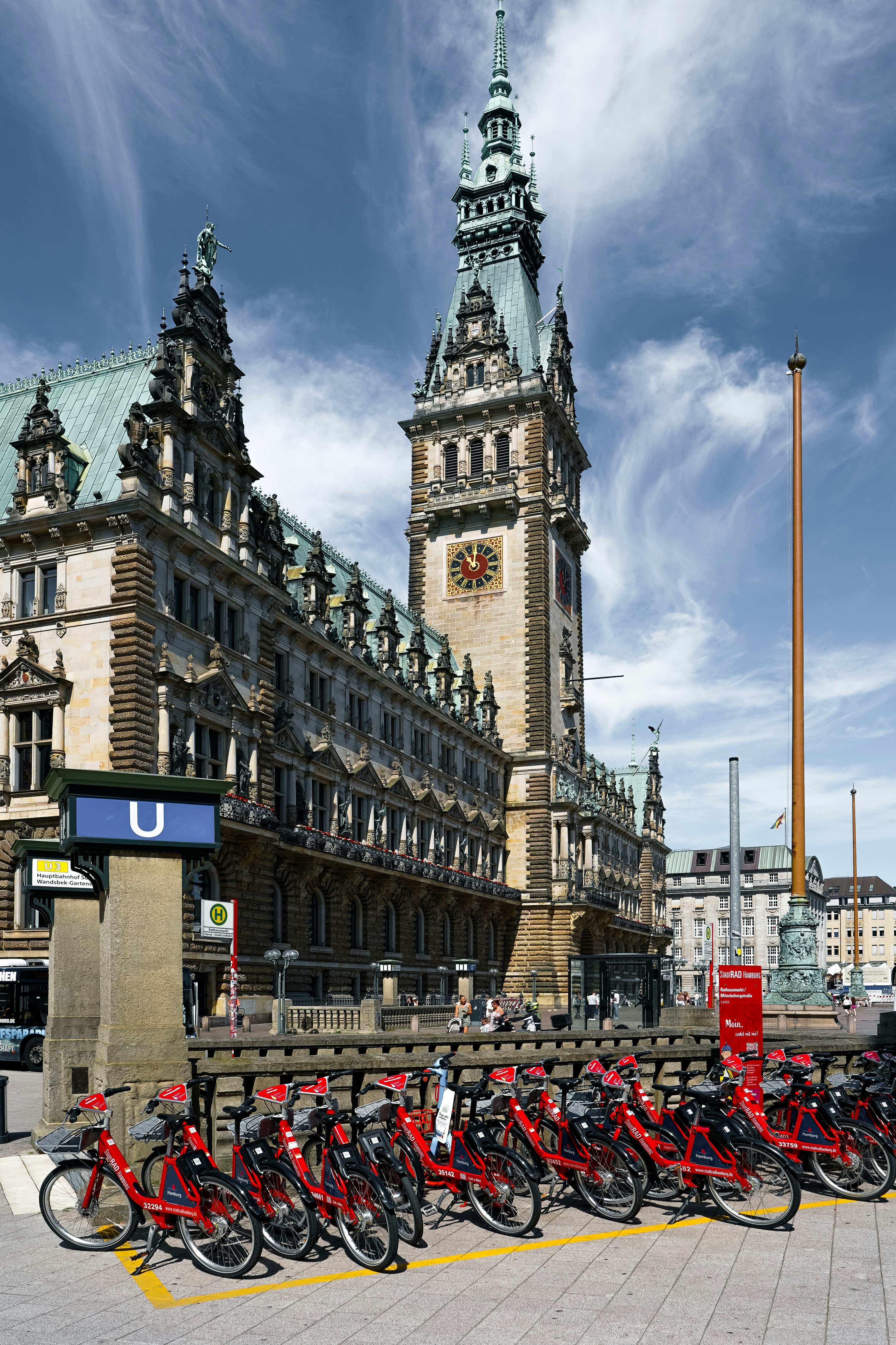 Una fila de bicicletas de alquiler rojas aparcada frente al ornamentado Ayuntamiento de Hamburgo