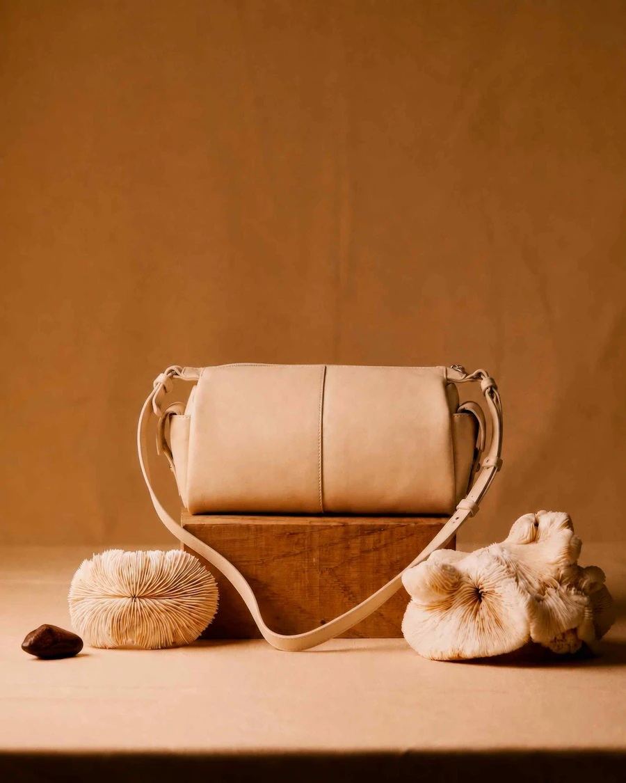 Beige leather crossbody bag on a wooden block against a tan wall