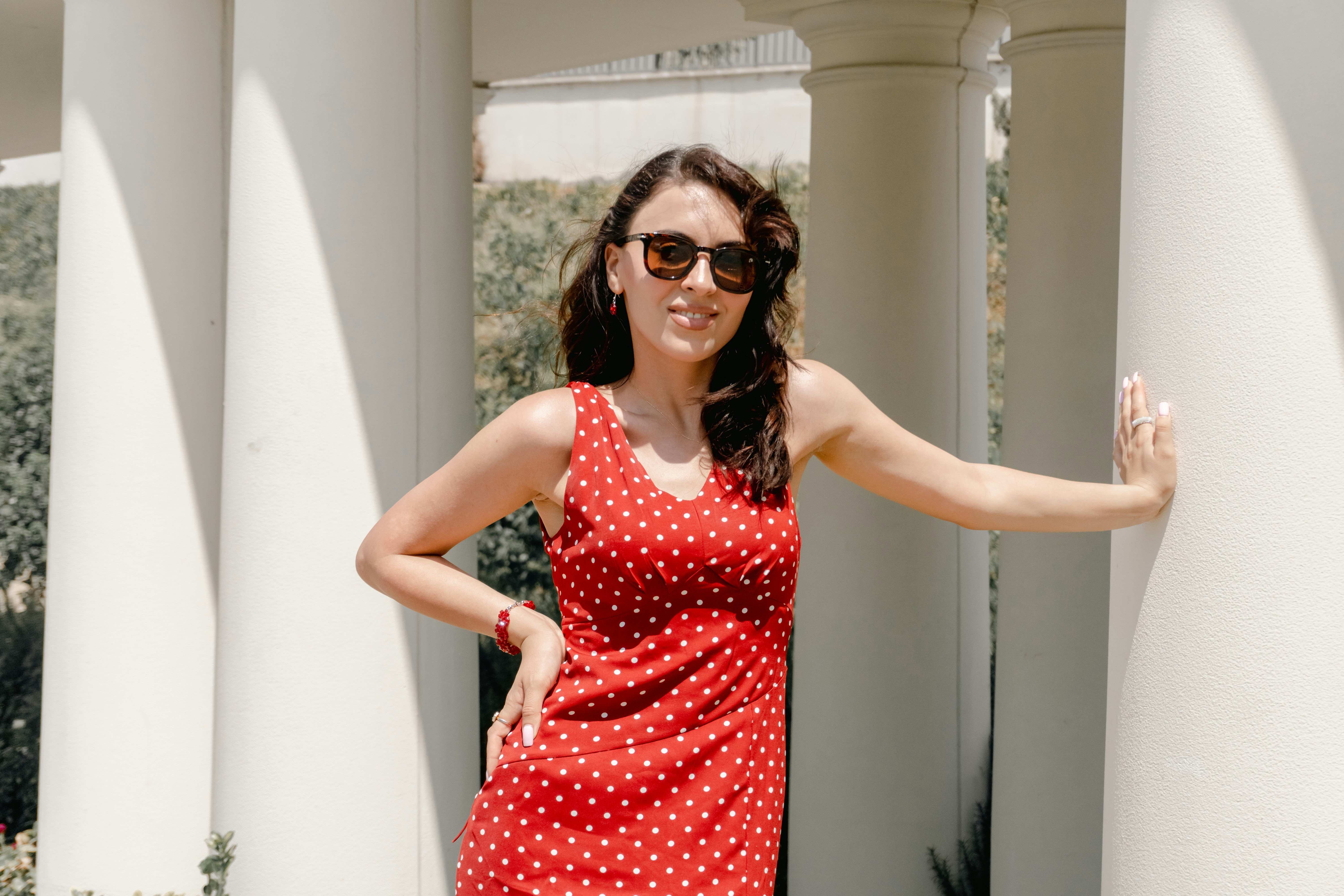 A woman in a red polka dot dress leaning against a white pillar