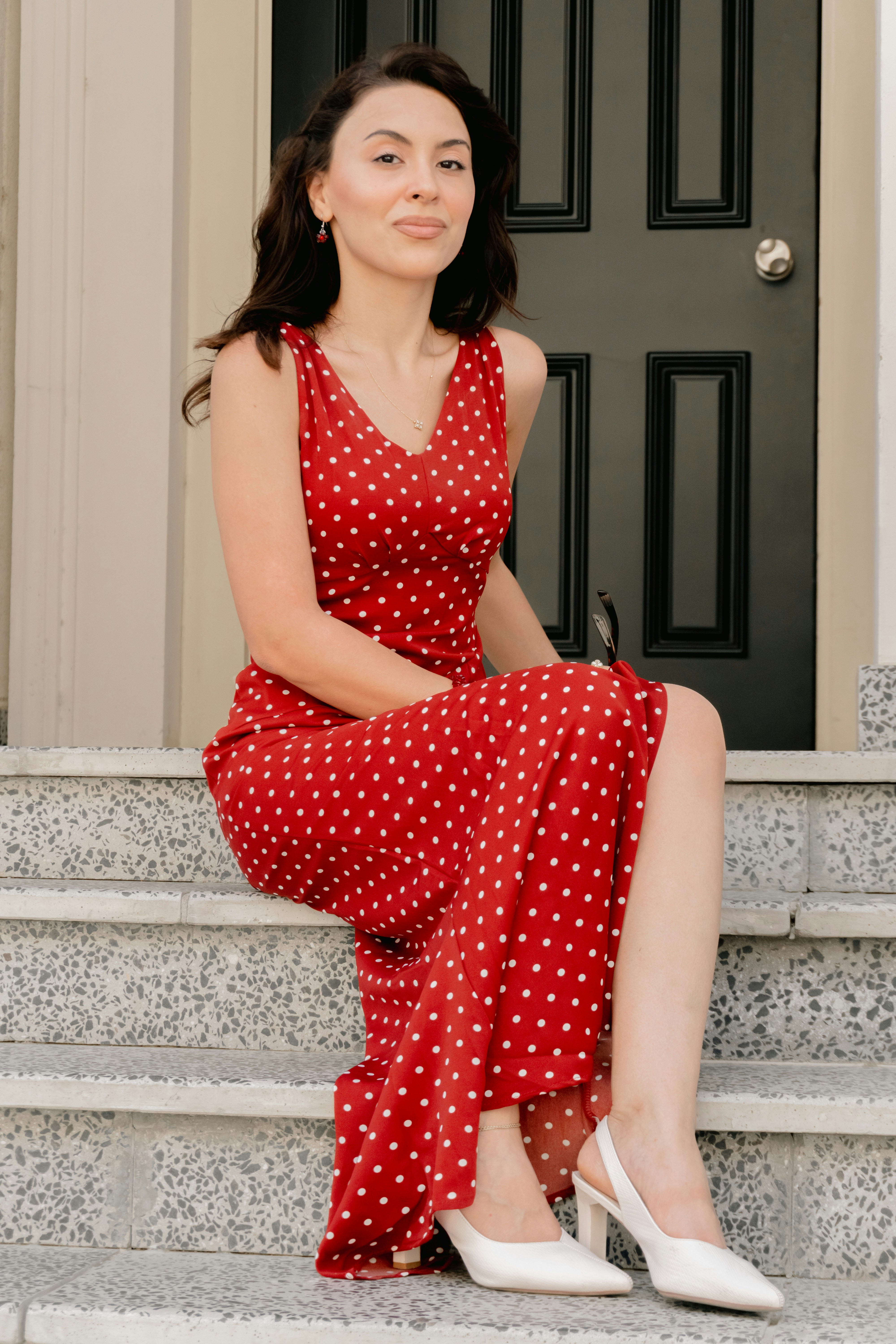 A woman in a red polka dot dress sitting on grey stone steps