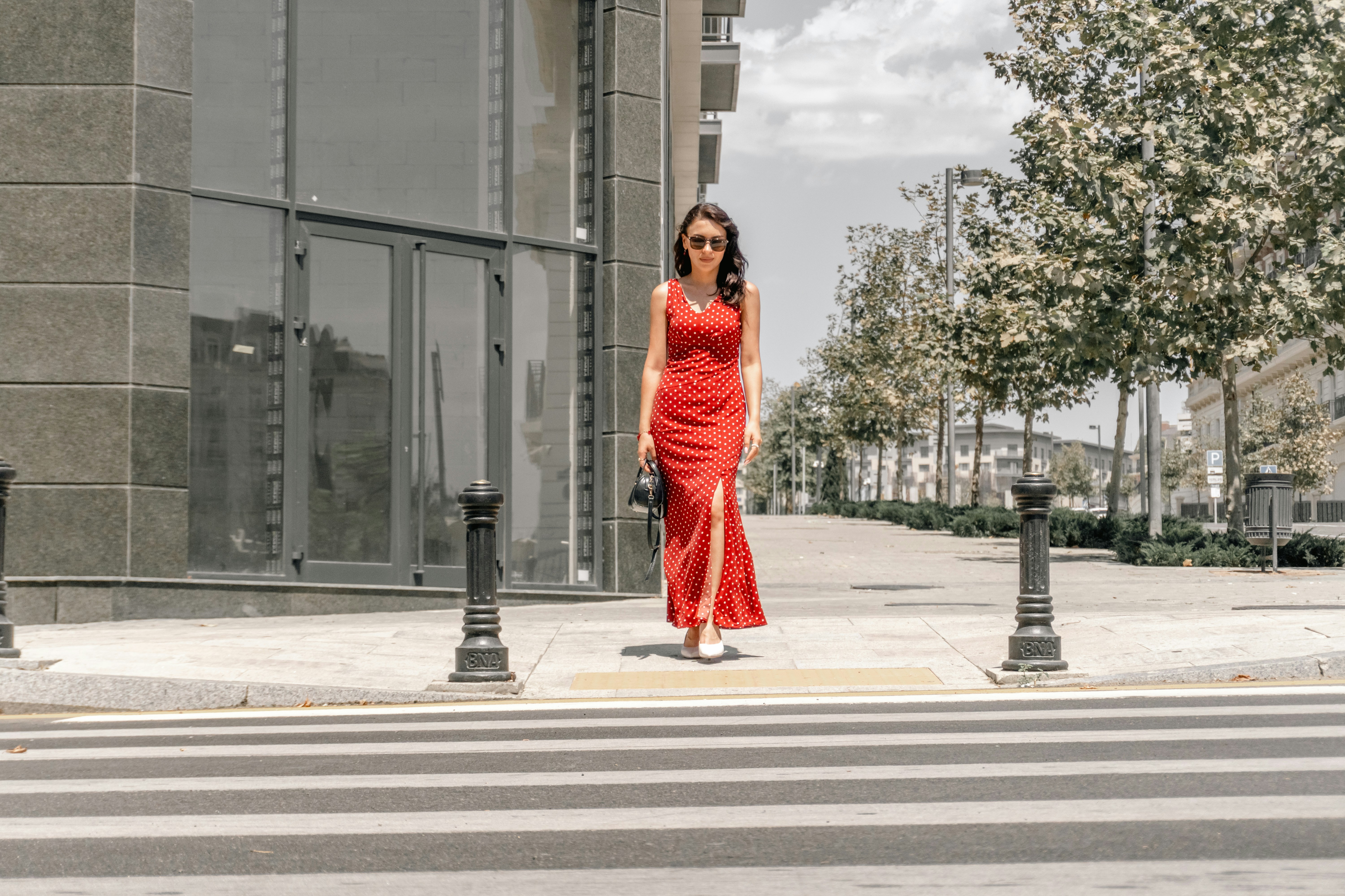 A woman in a red polka dot dress walking across a city crosswalk