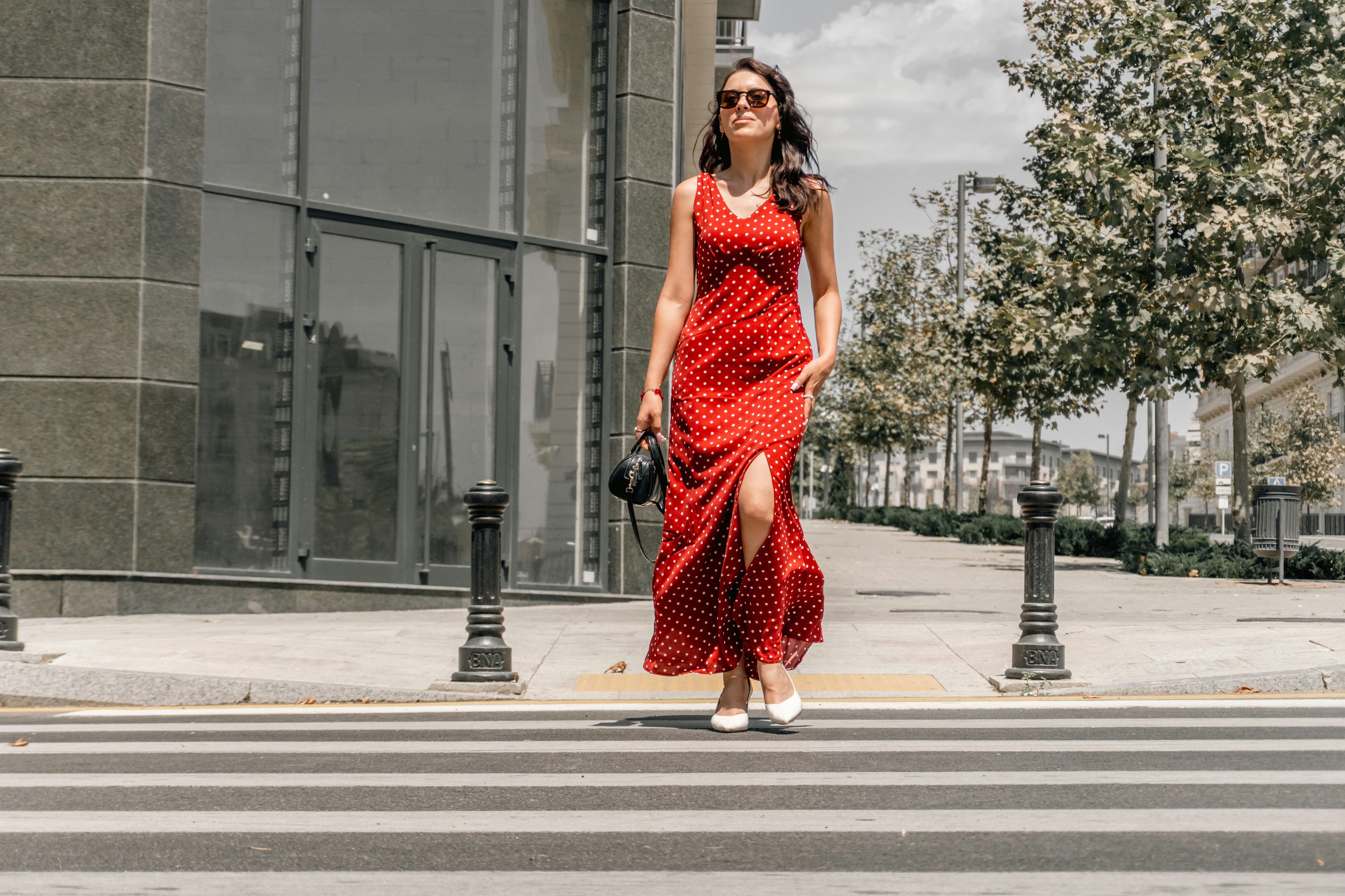 A woman in a red polka dot dress walking across a city crosswalk