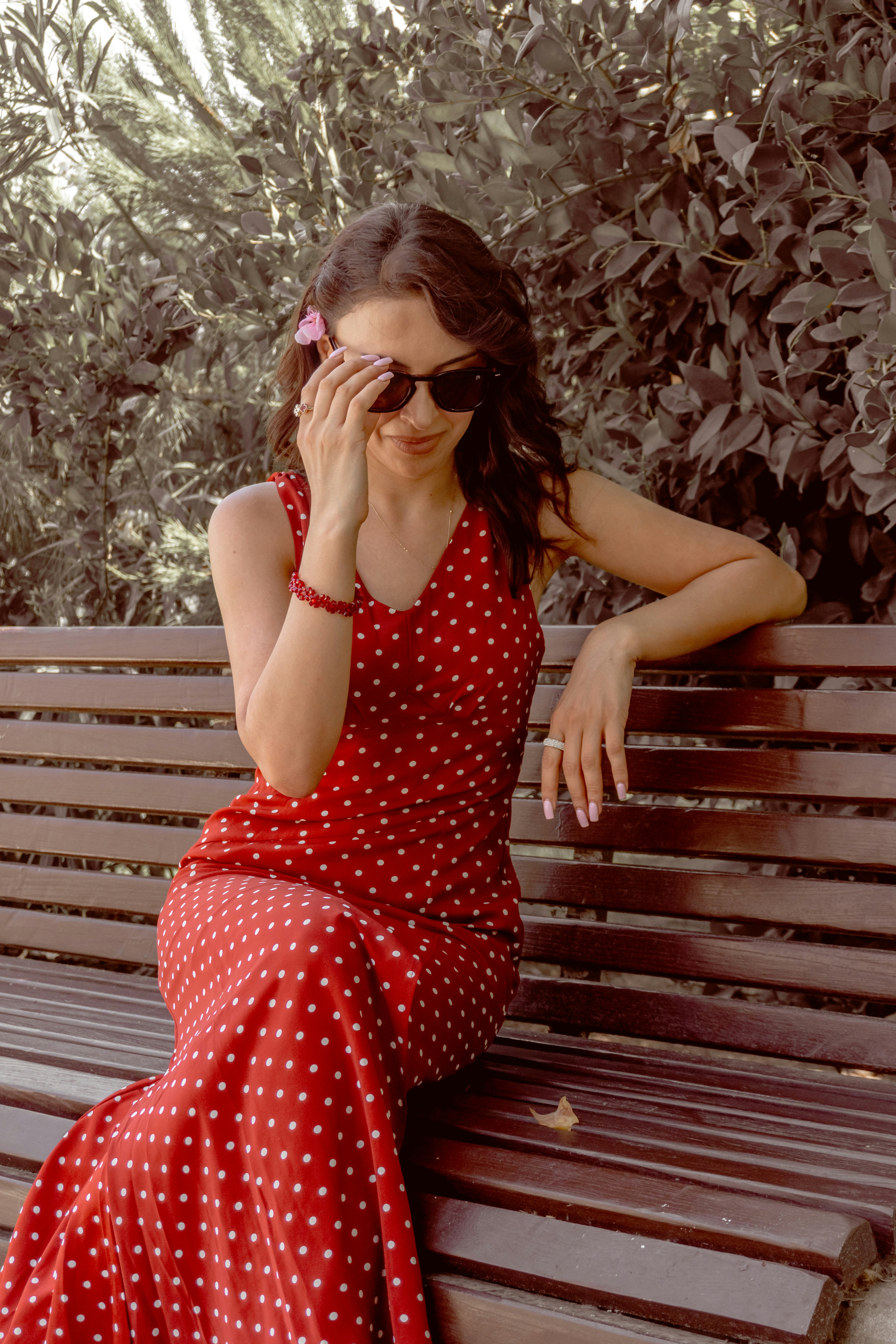 A woman in a red polka dot dress sitting on a wooden bench