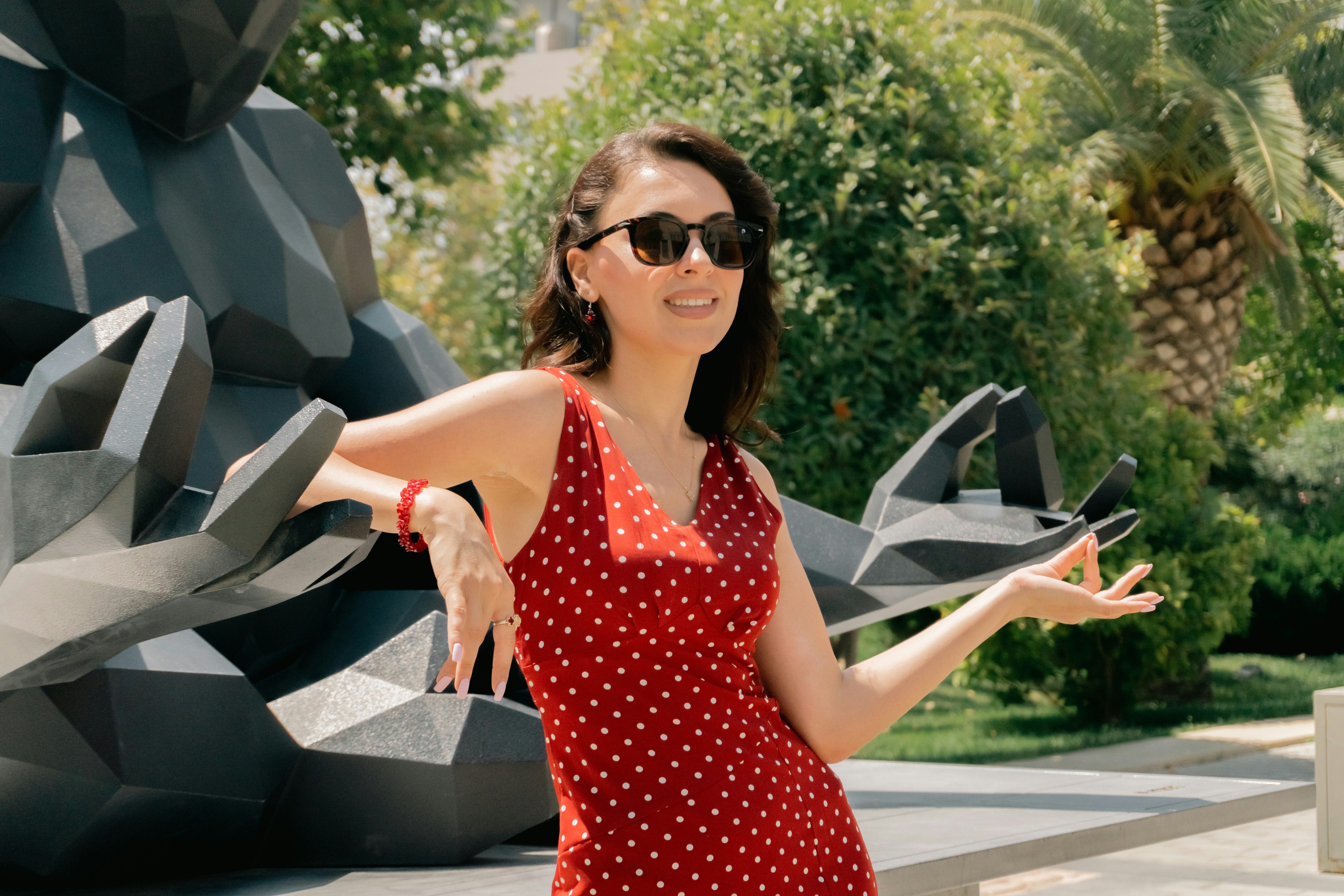 A woman in a red polka dot dress leaning against a dark geometric sculpture