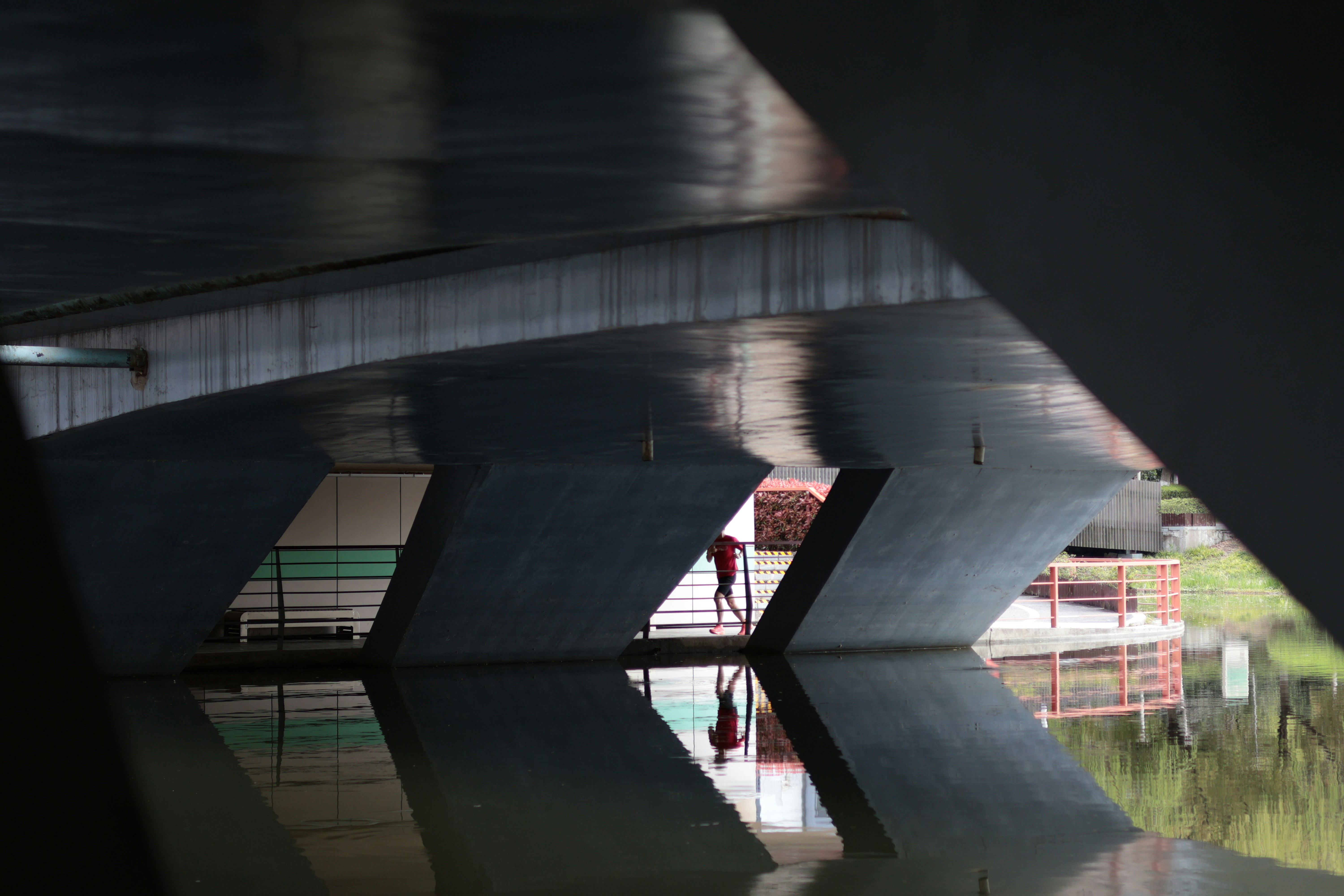 A person in a red shirt running under a concrete bridge over water