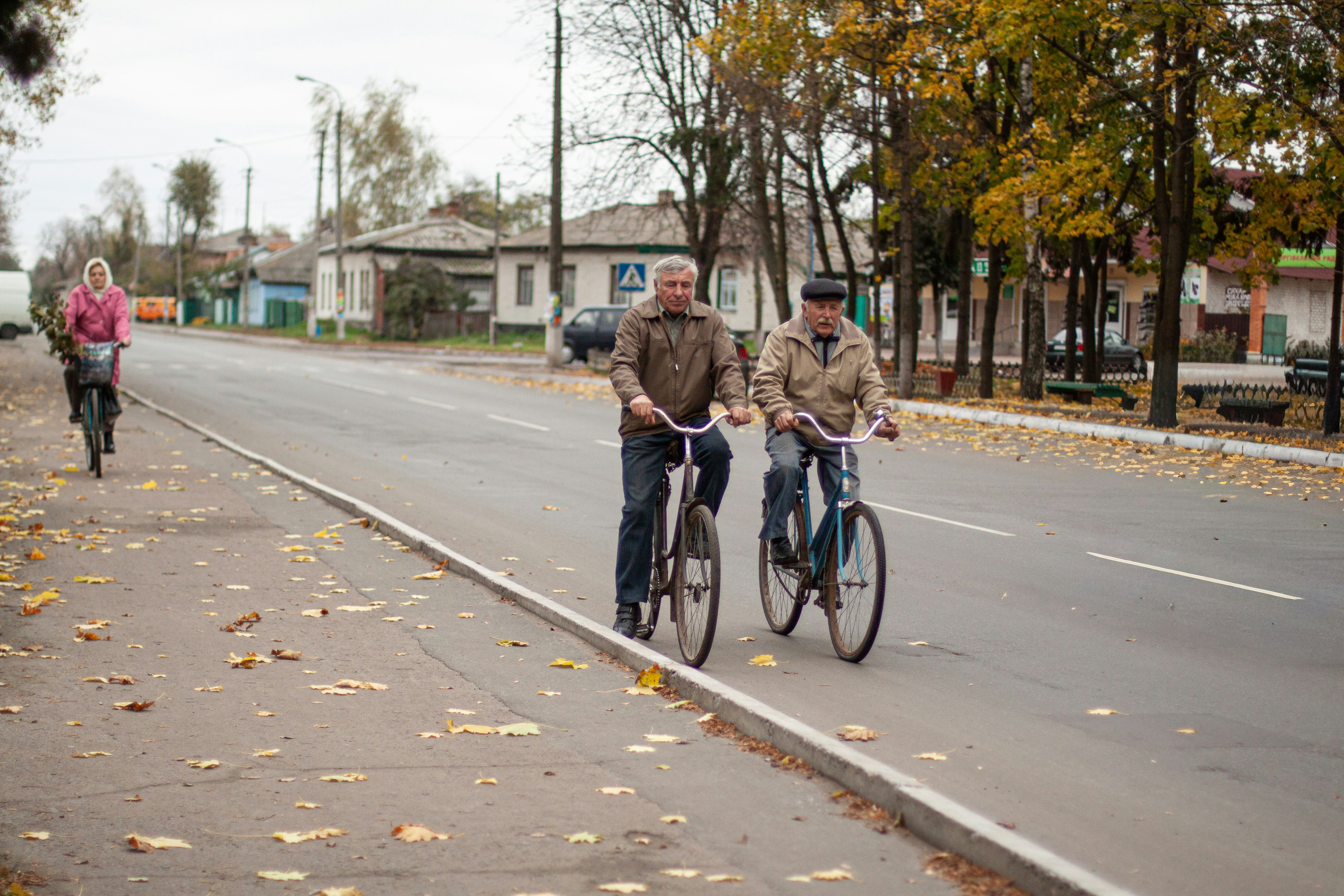 Two men cycling on a road with a woman riding behind them in autumn