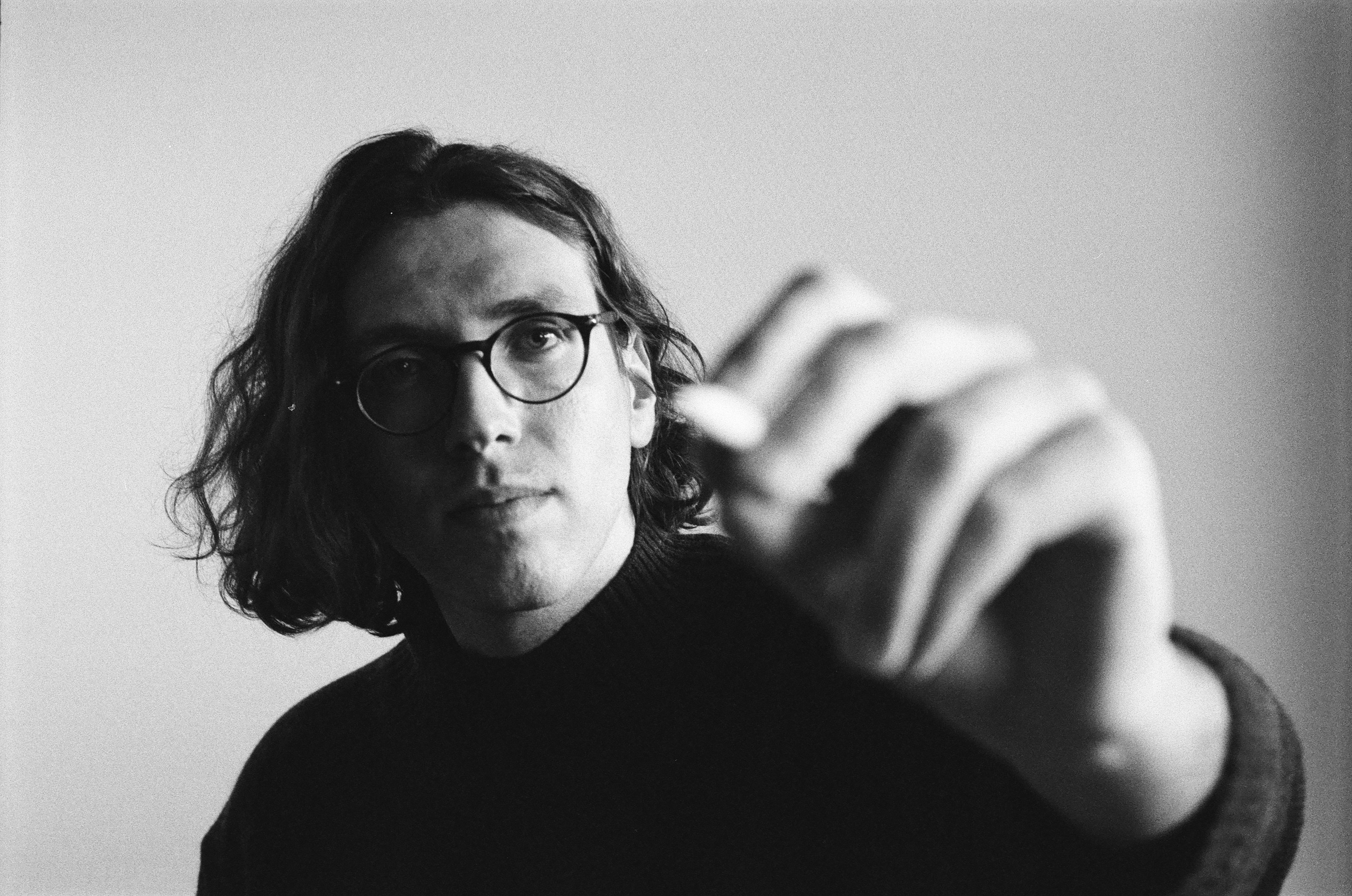A person with long hair and glasses reaching toward the camera