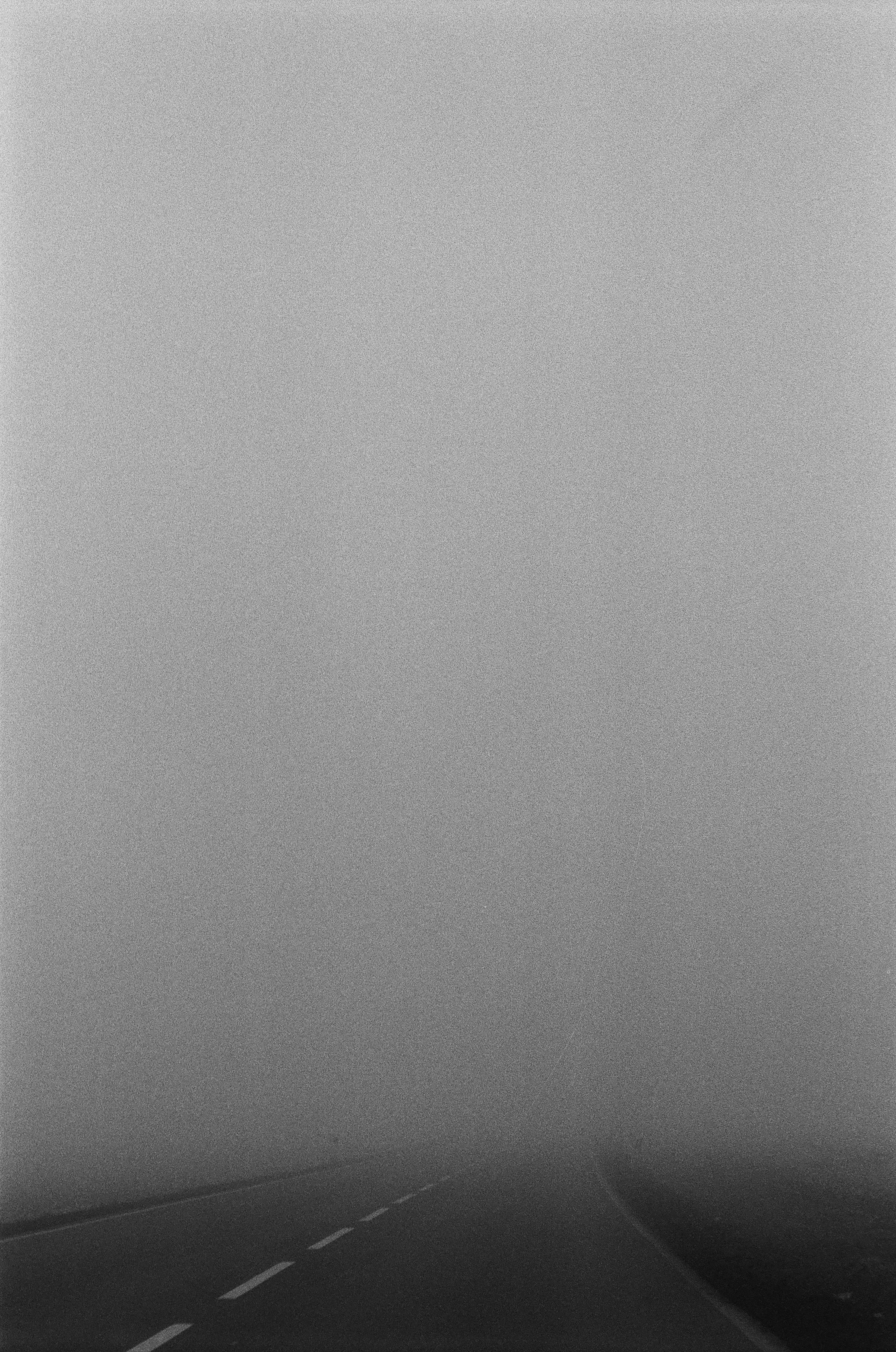 A dark asphalt road with white lane markings disappearing into thick grey fog