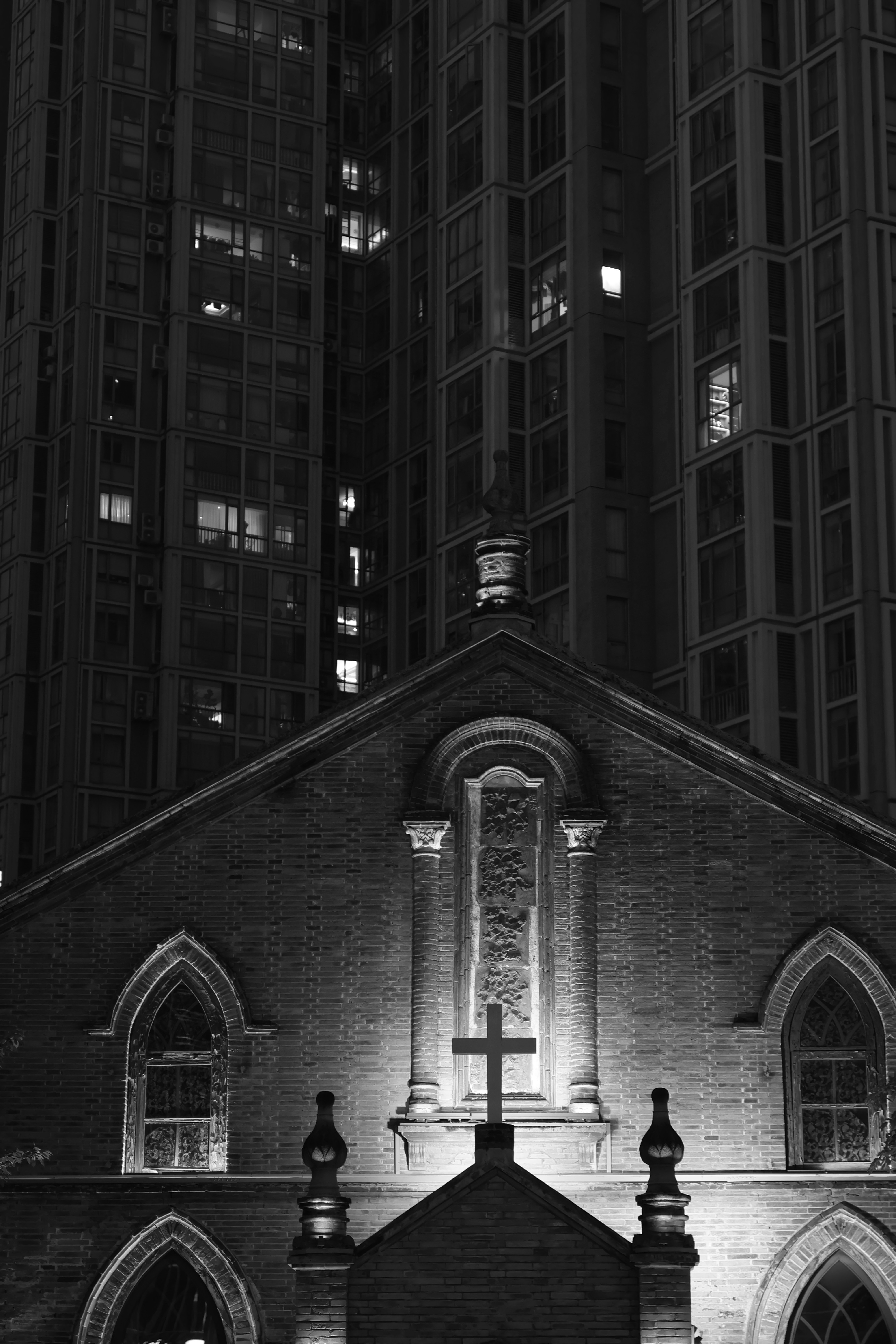 A stone church with a cross against a tall modern apartment building at night