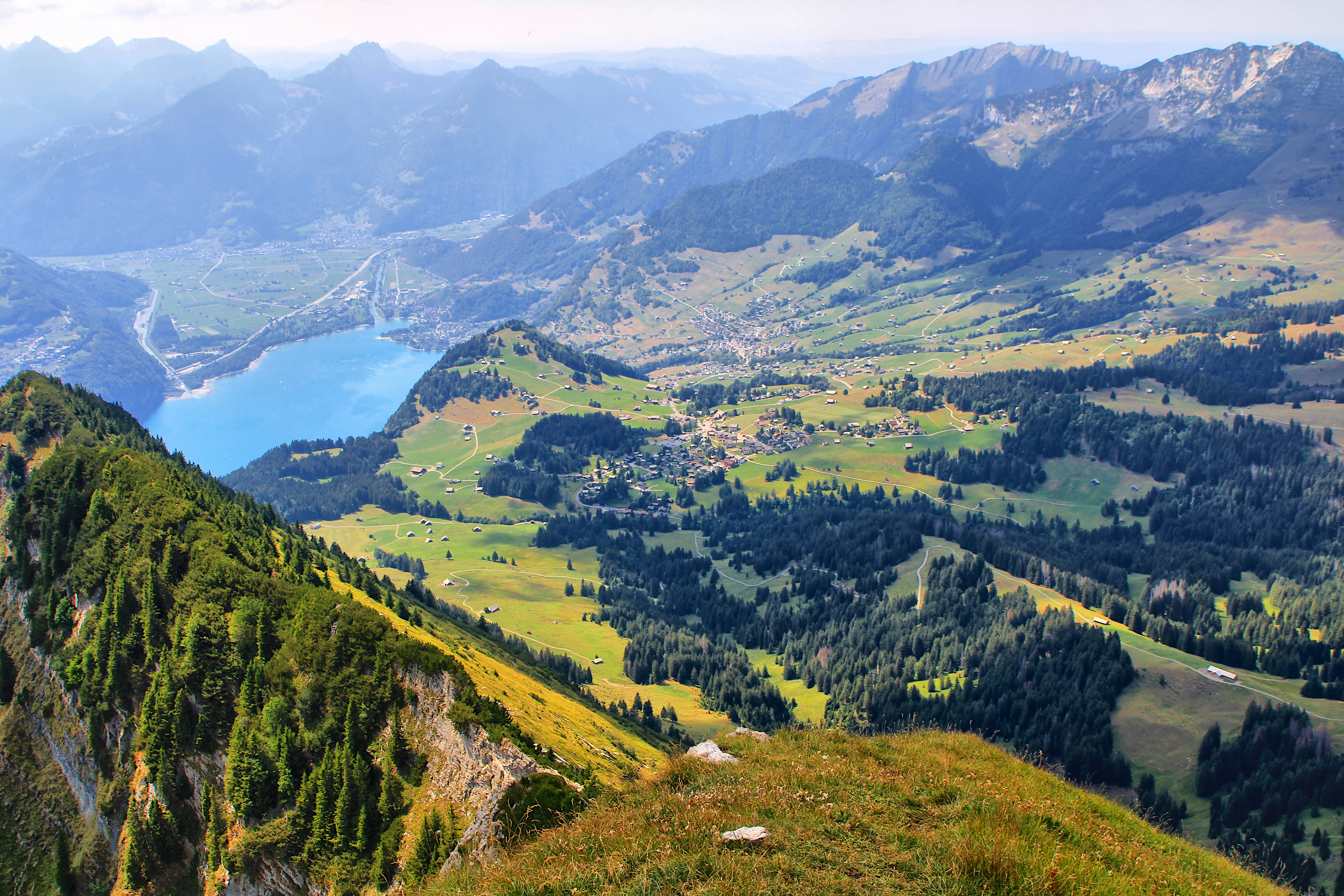 A high mountain view overlooking a green valley with a lake and village | Houfy — Book Direct