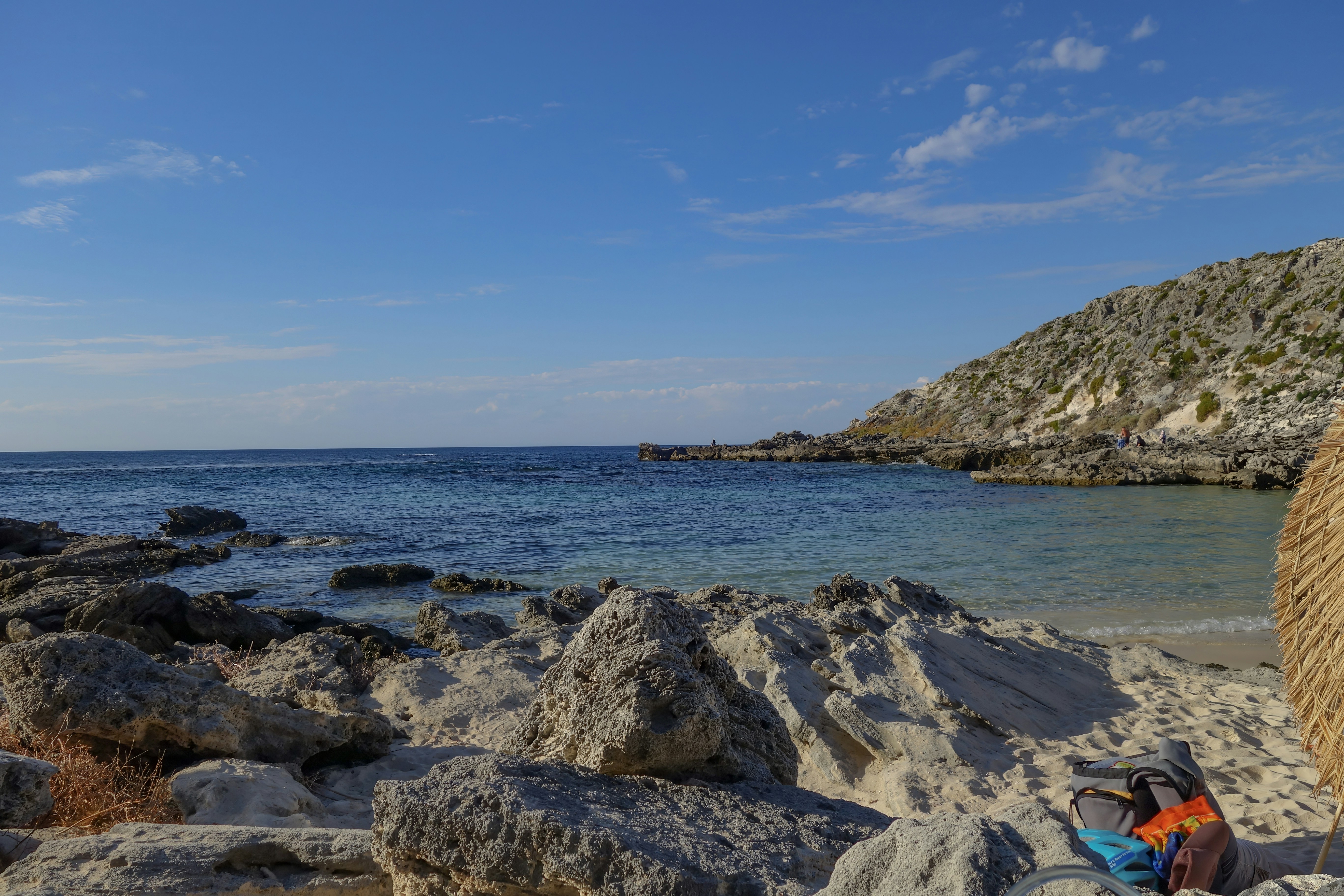 A rocky beach with a small sandy cove under a clear blue sky