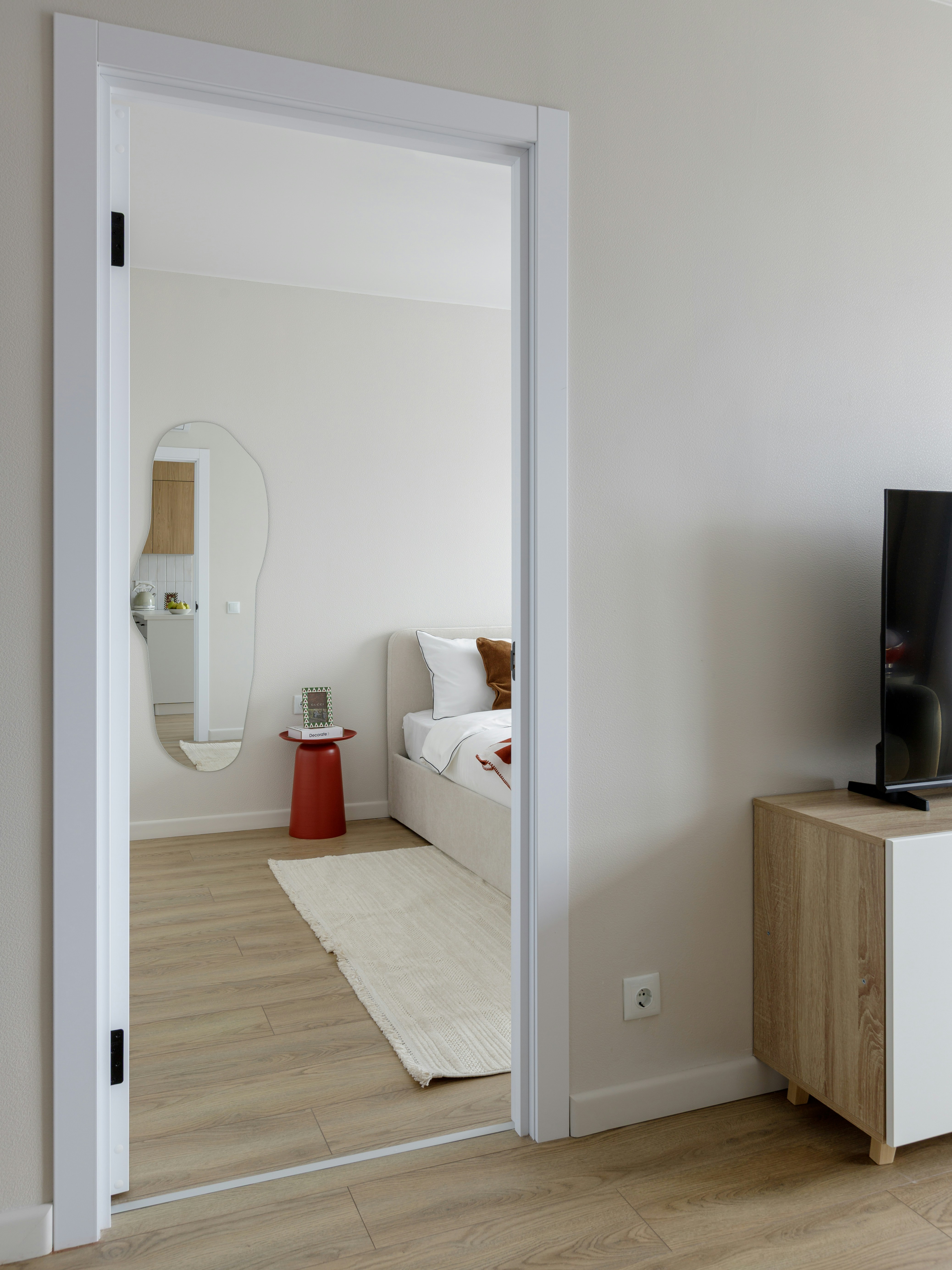 A view through a doorway into a bedroom with a bed and red side table