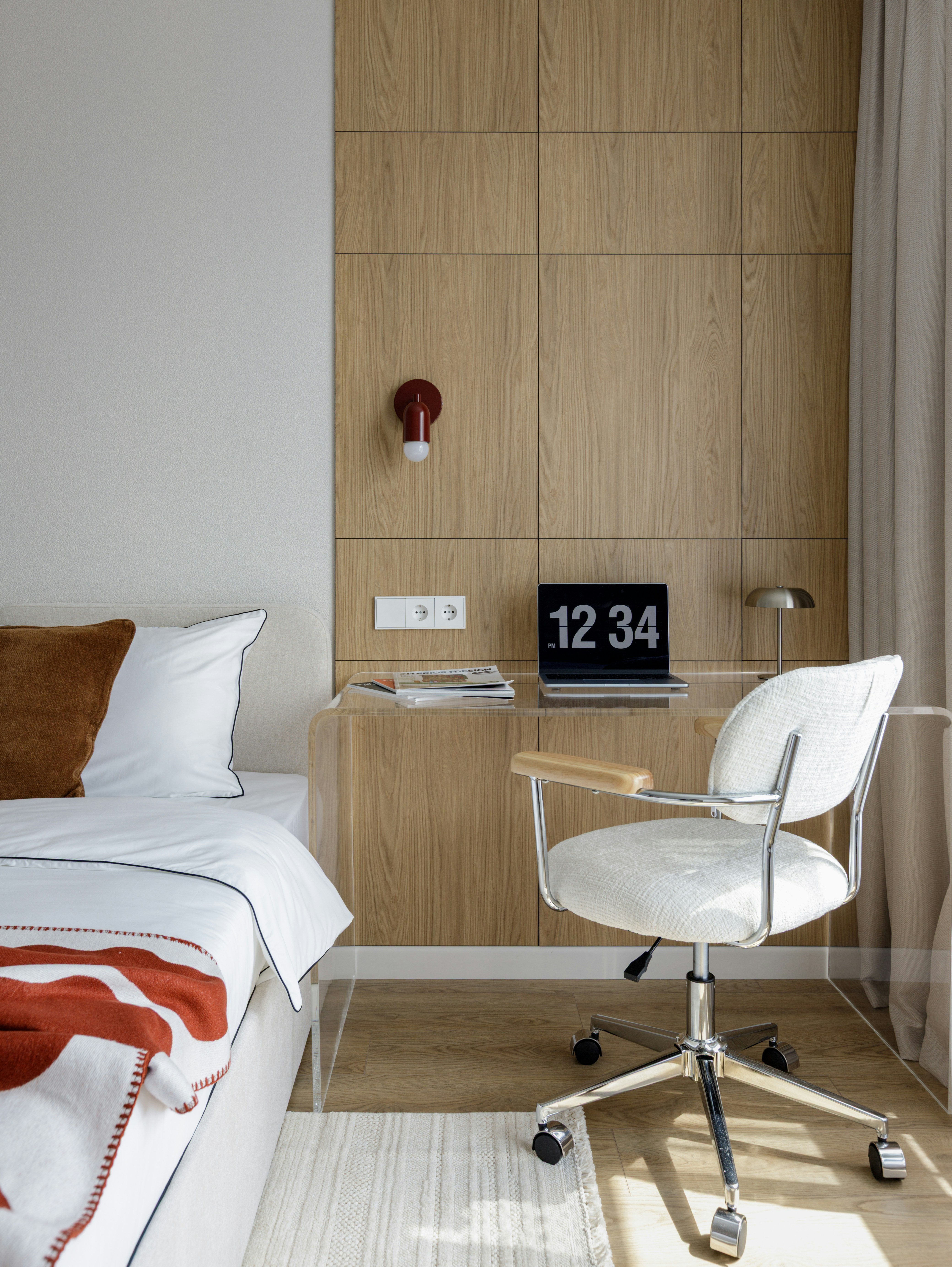 A laptop on a clear desk beside a bed in a modern bedroom