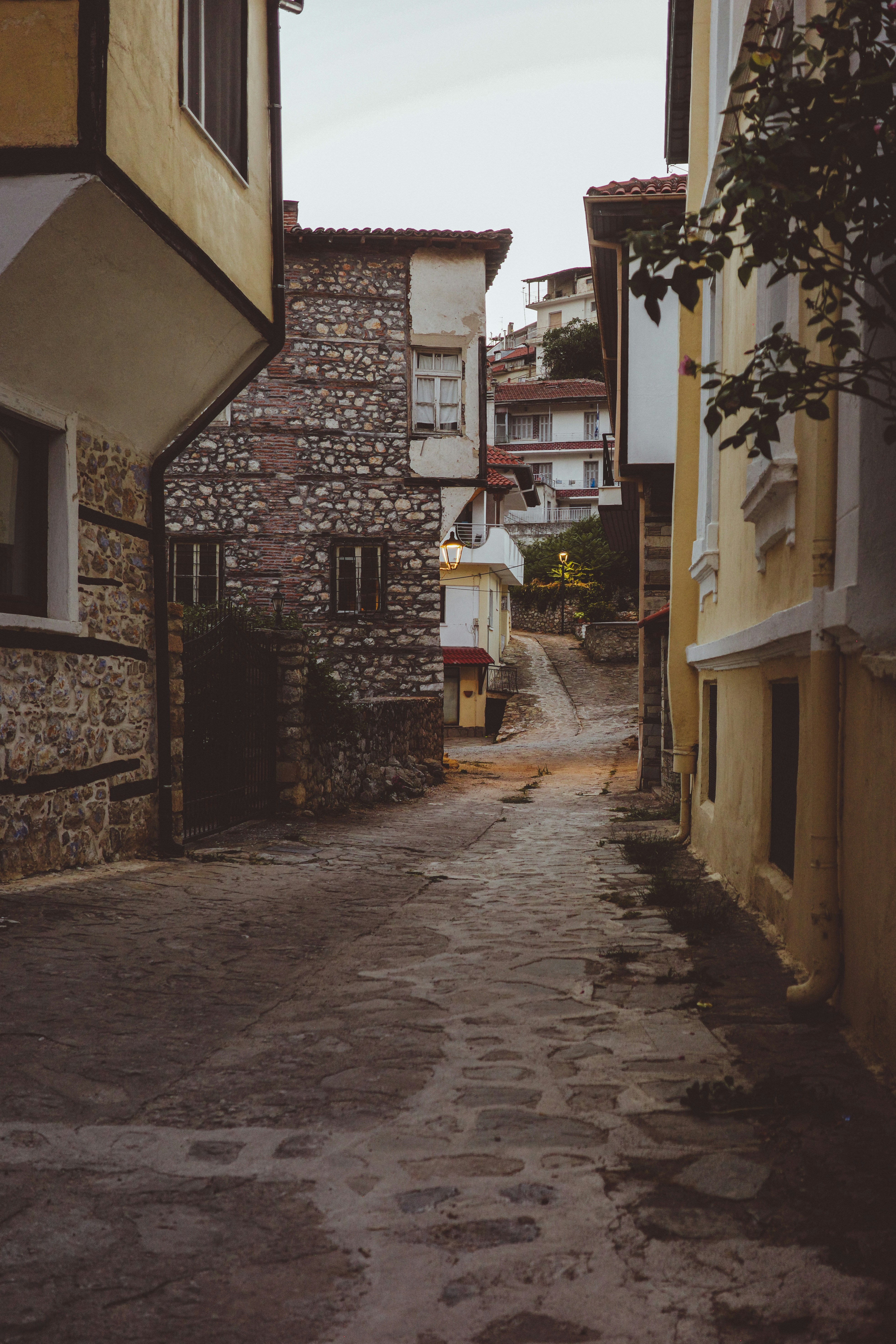 A narrow cobblestone street between old stone and yellow stucco buildings at dusk