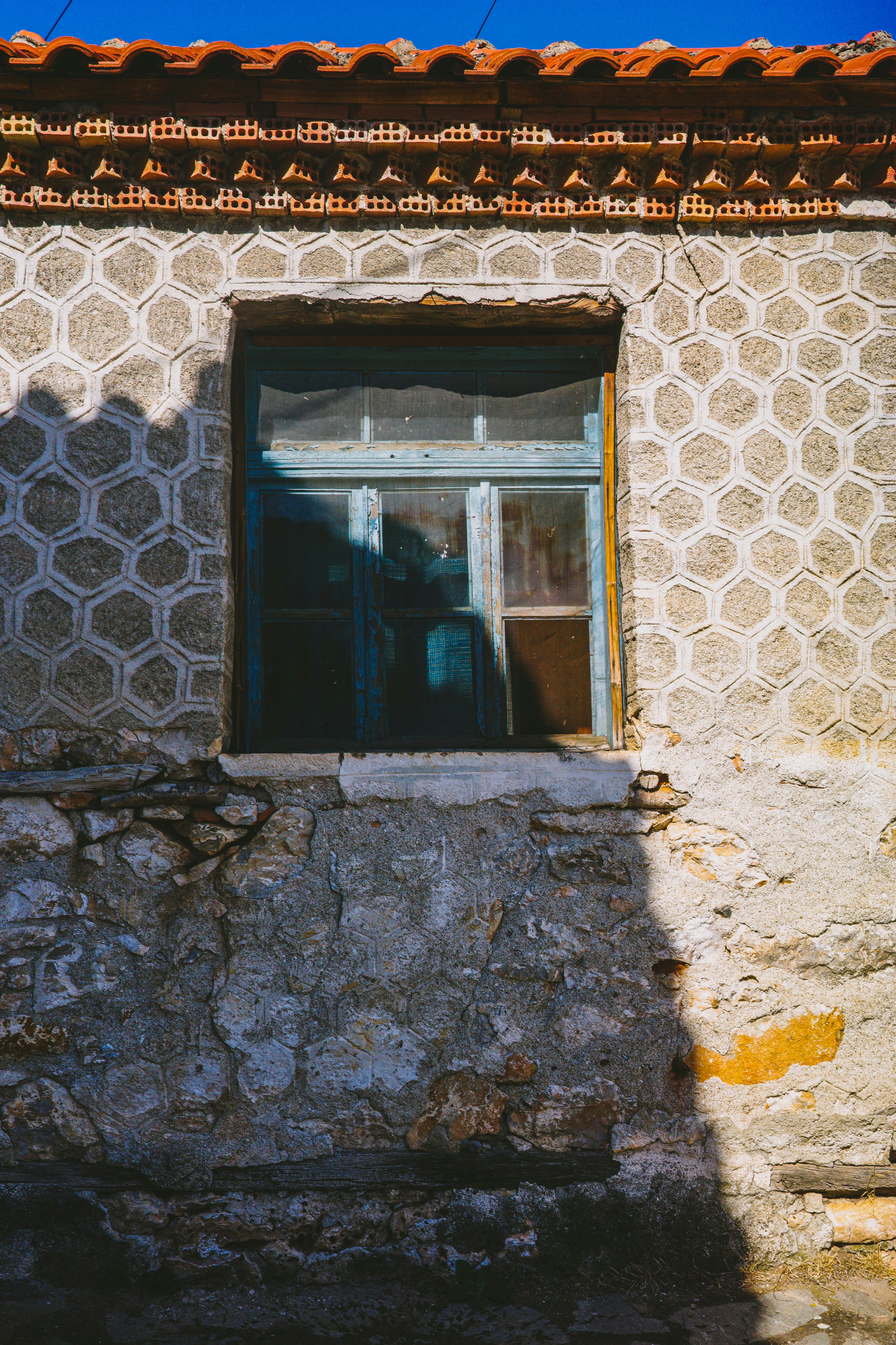 A weathered blue window frame set in a stone wall with hexagonal patterns
