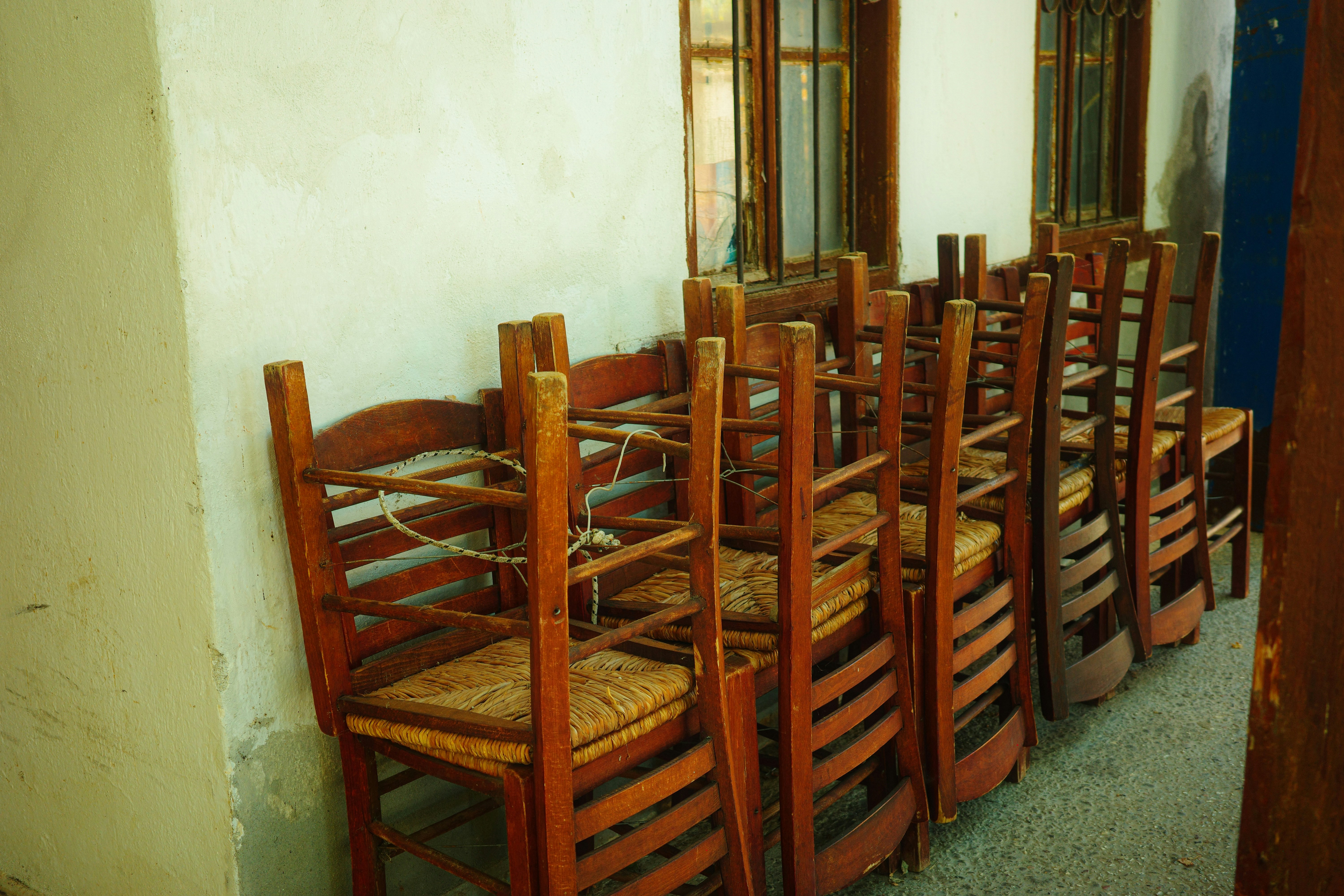 A row of wooden chairs with woven seats stacked against a white wall