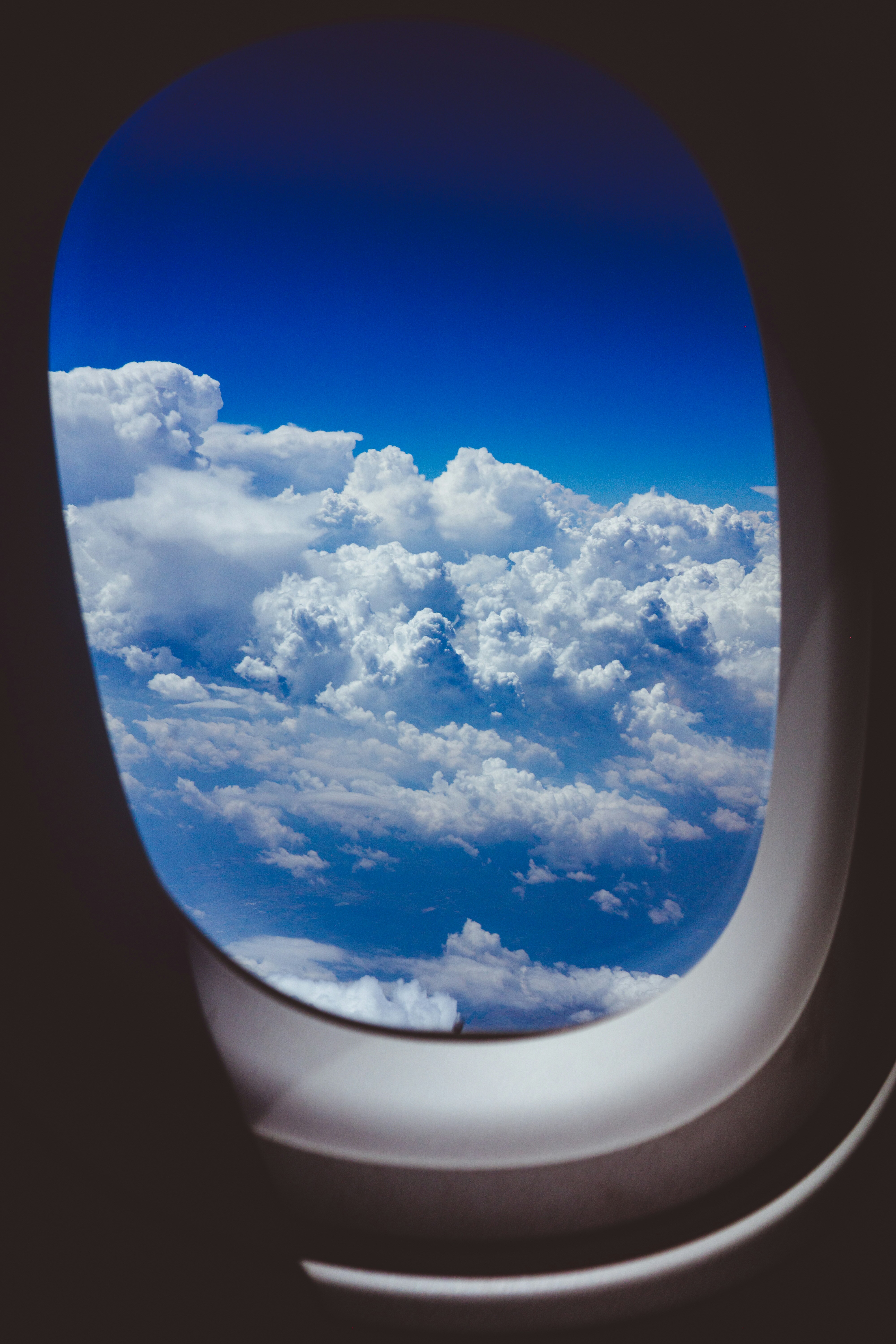 Fluffy white clouds against a deep blue sky viewed through an airplane window