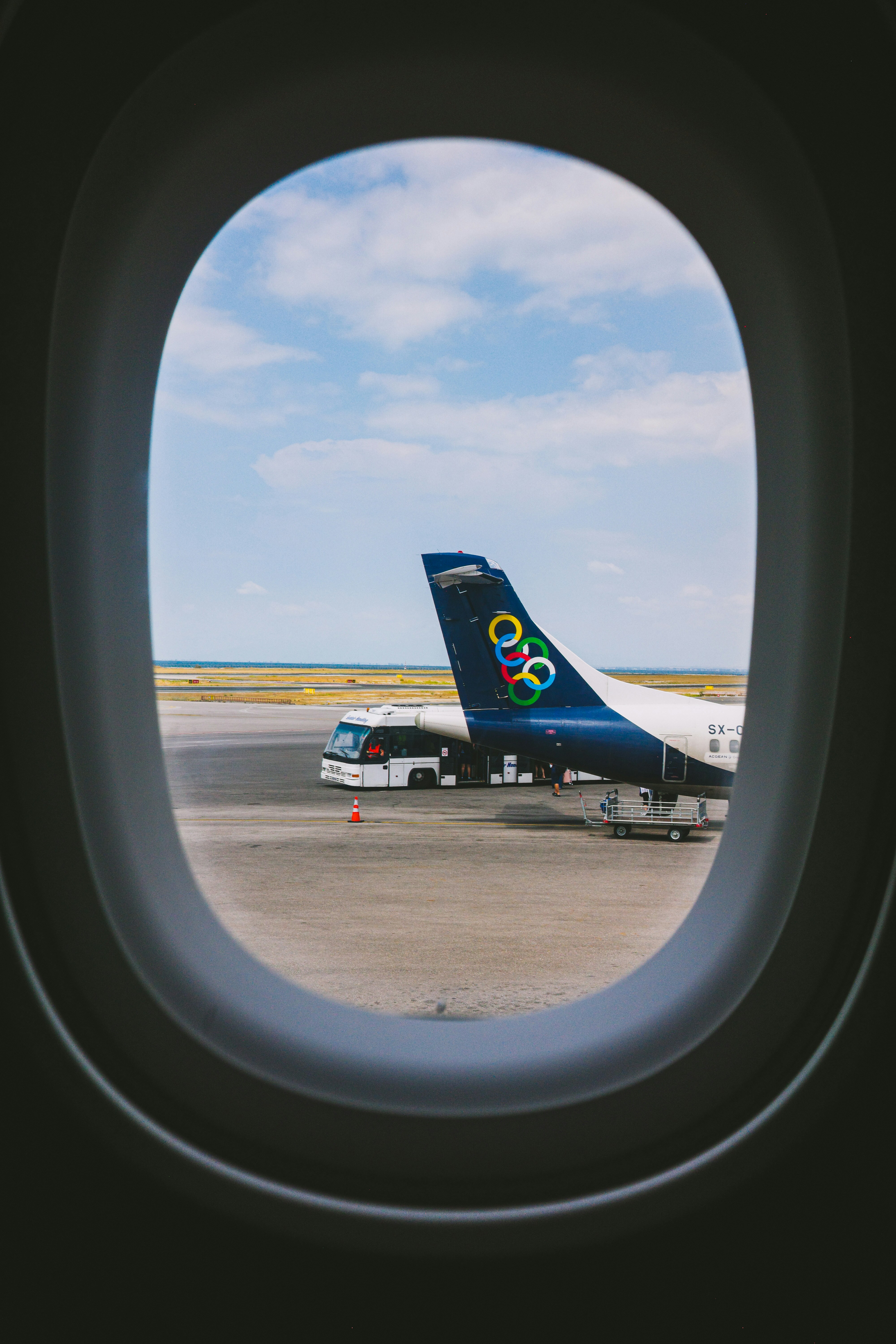 View through an airplane window of an aircraft tail and shuttle bus on tarmac
