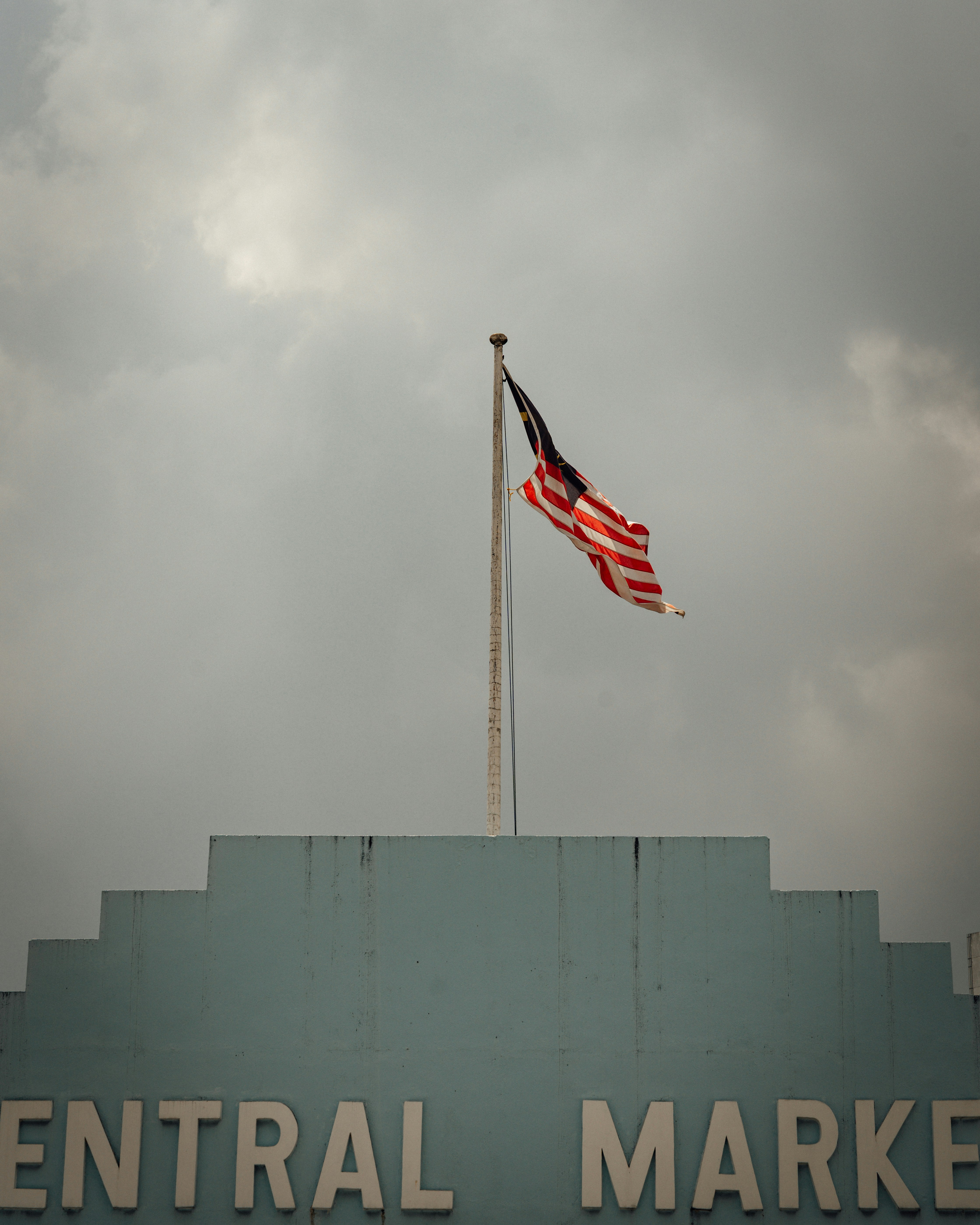The Malaysian flag flying above the Central Market building under a cloudy sky