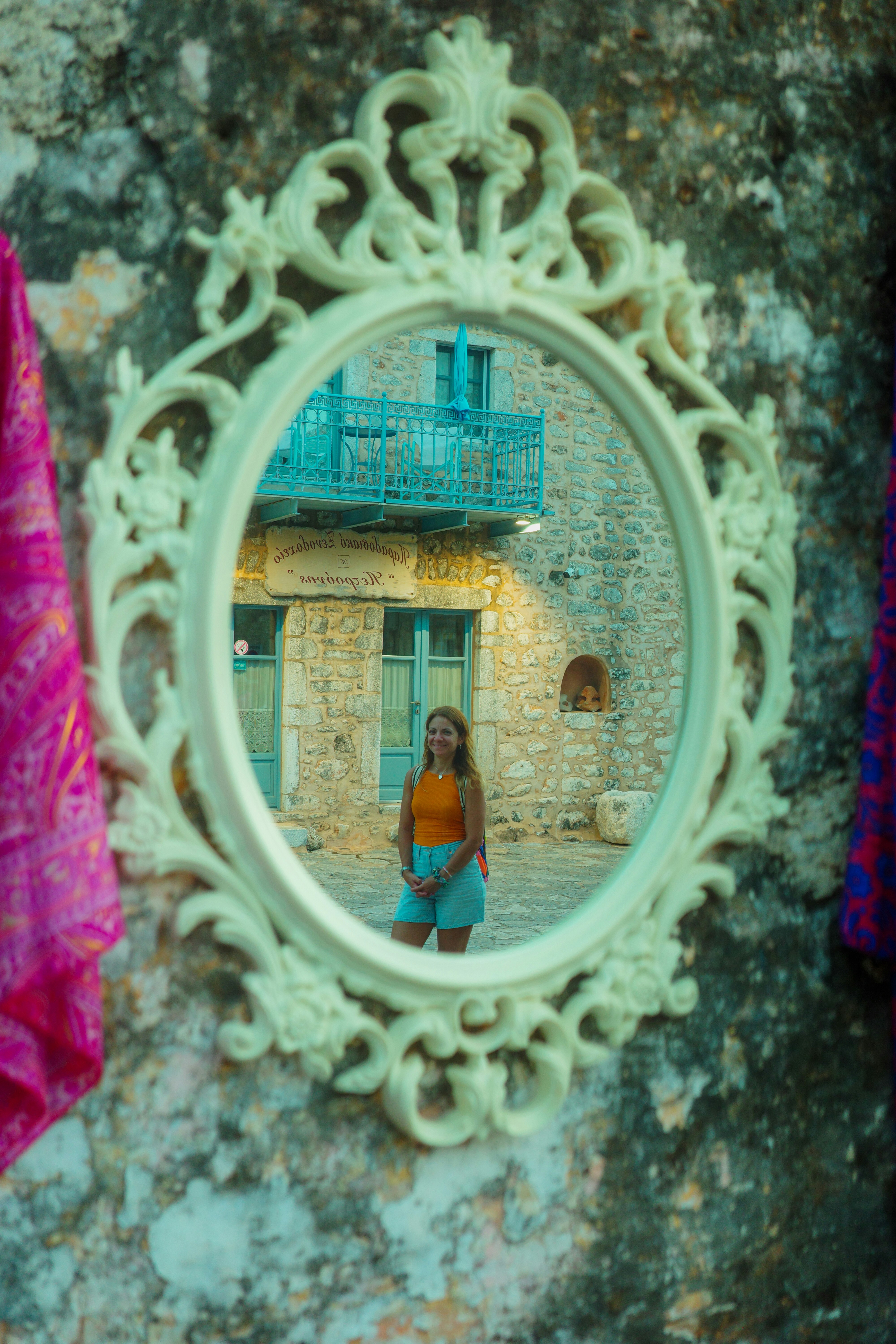 A woman in an orange top reflected in an ornate white oval mirror