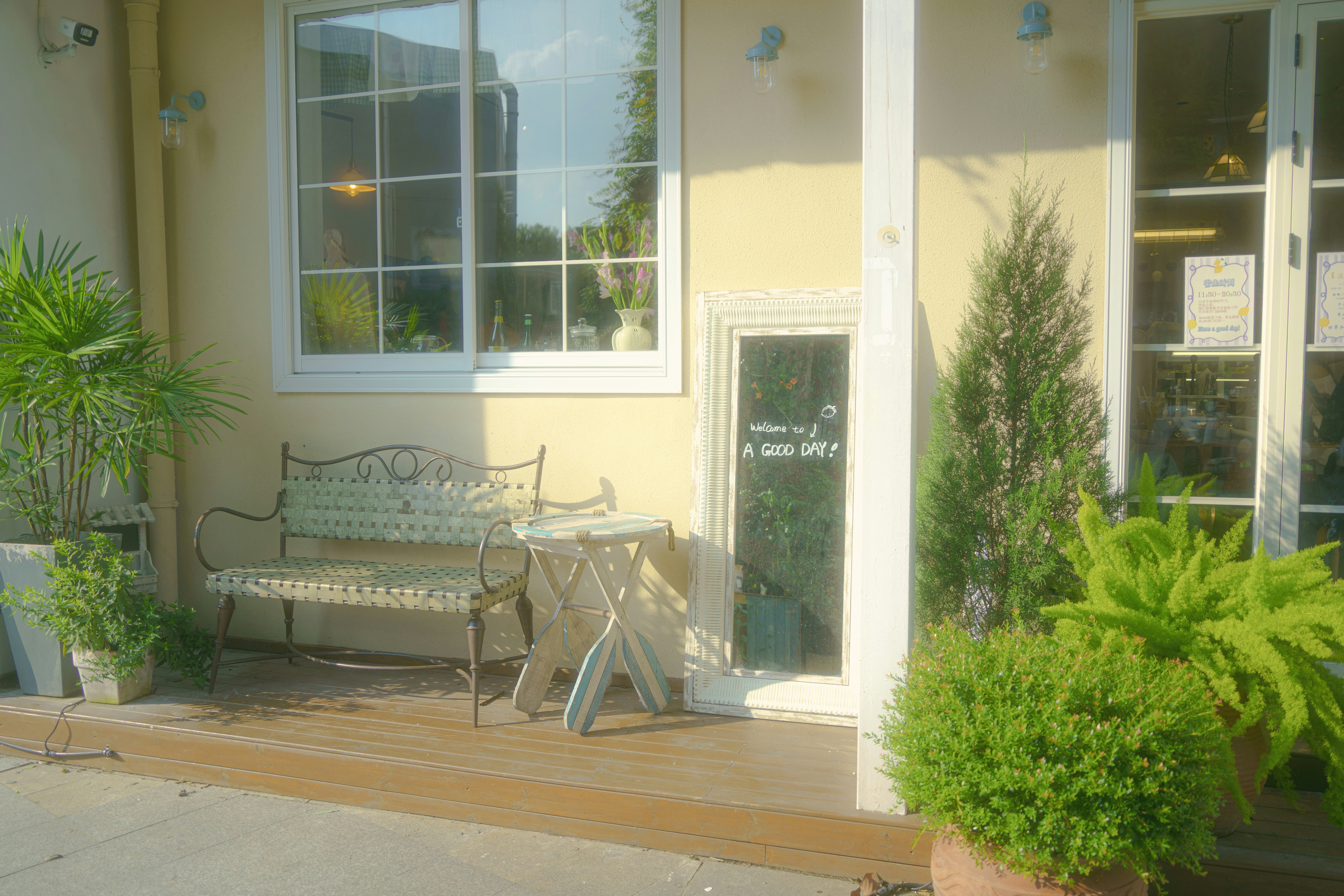 A metal bench and small table on a wooden porch with potted plants