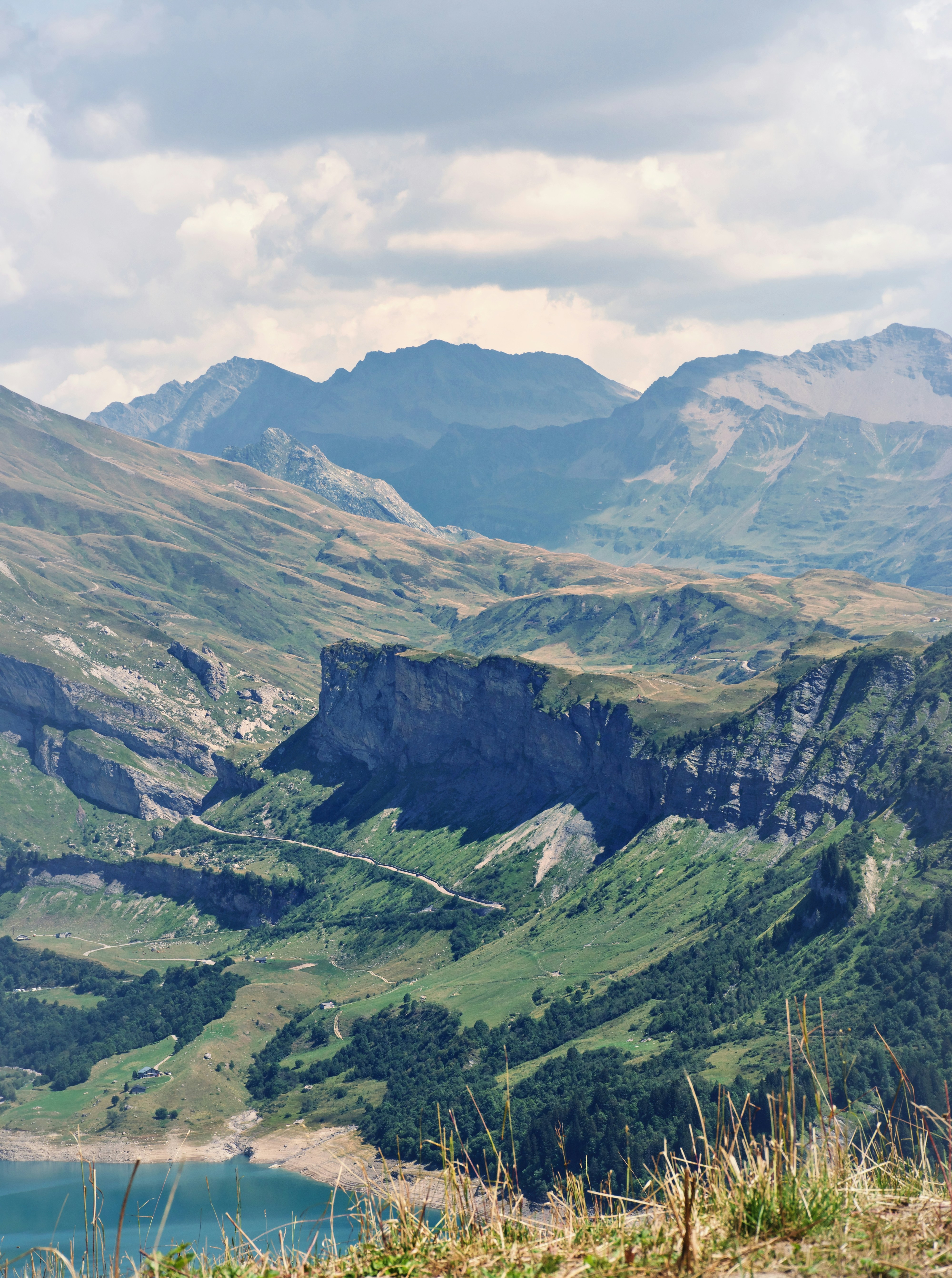 A winding road through a green mountain valley with a lake below