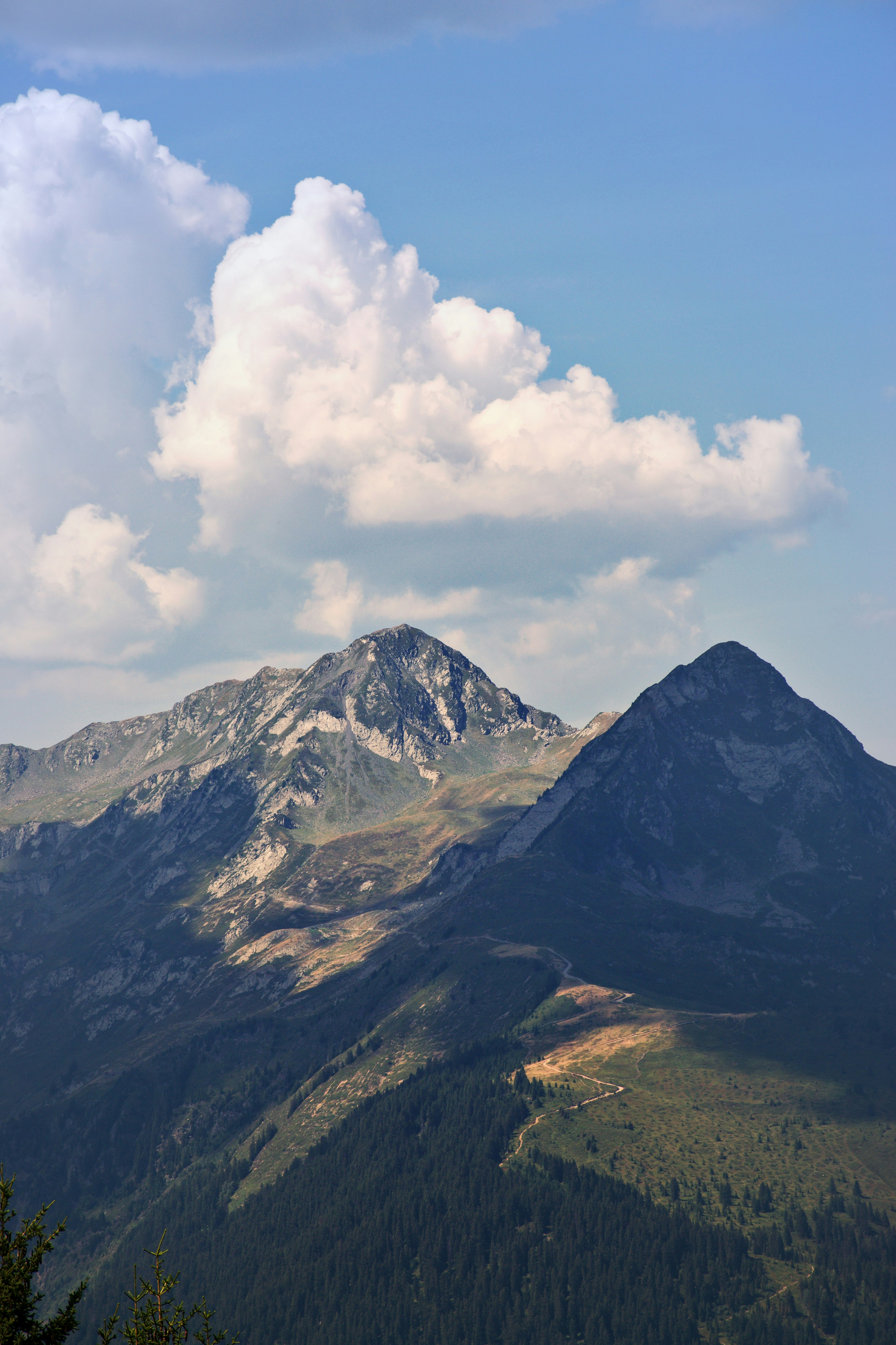 Two rocky mountain peaks under a bright blue sky with large white clouds