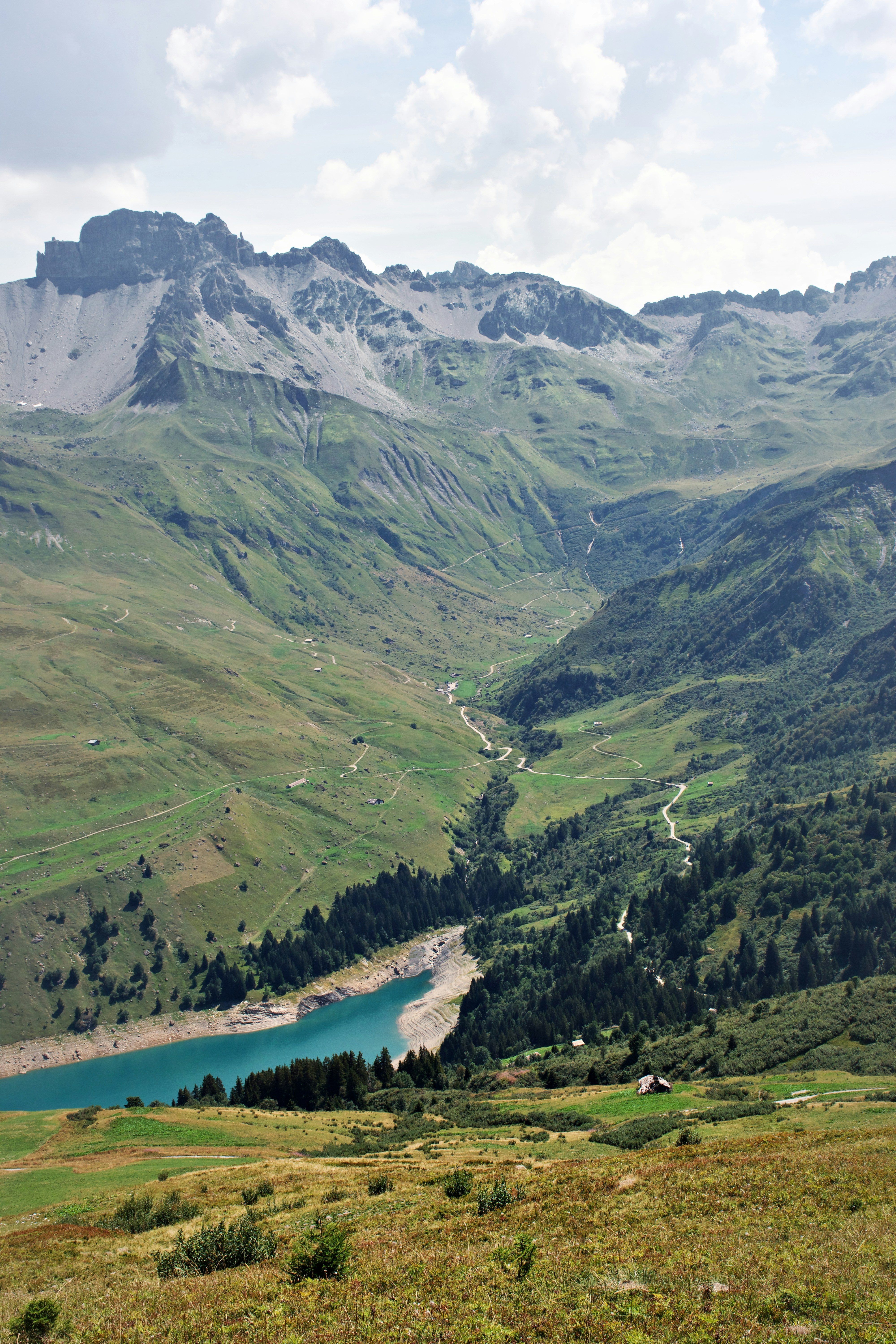 A turquoise alpine lake in a deep green valley below jagged mountain peaks