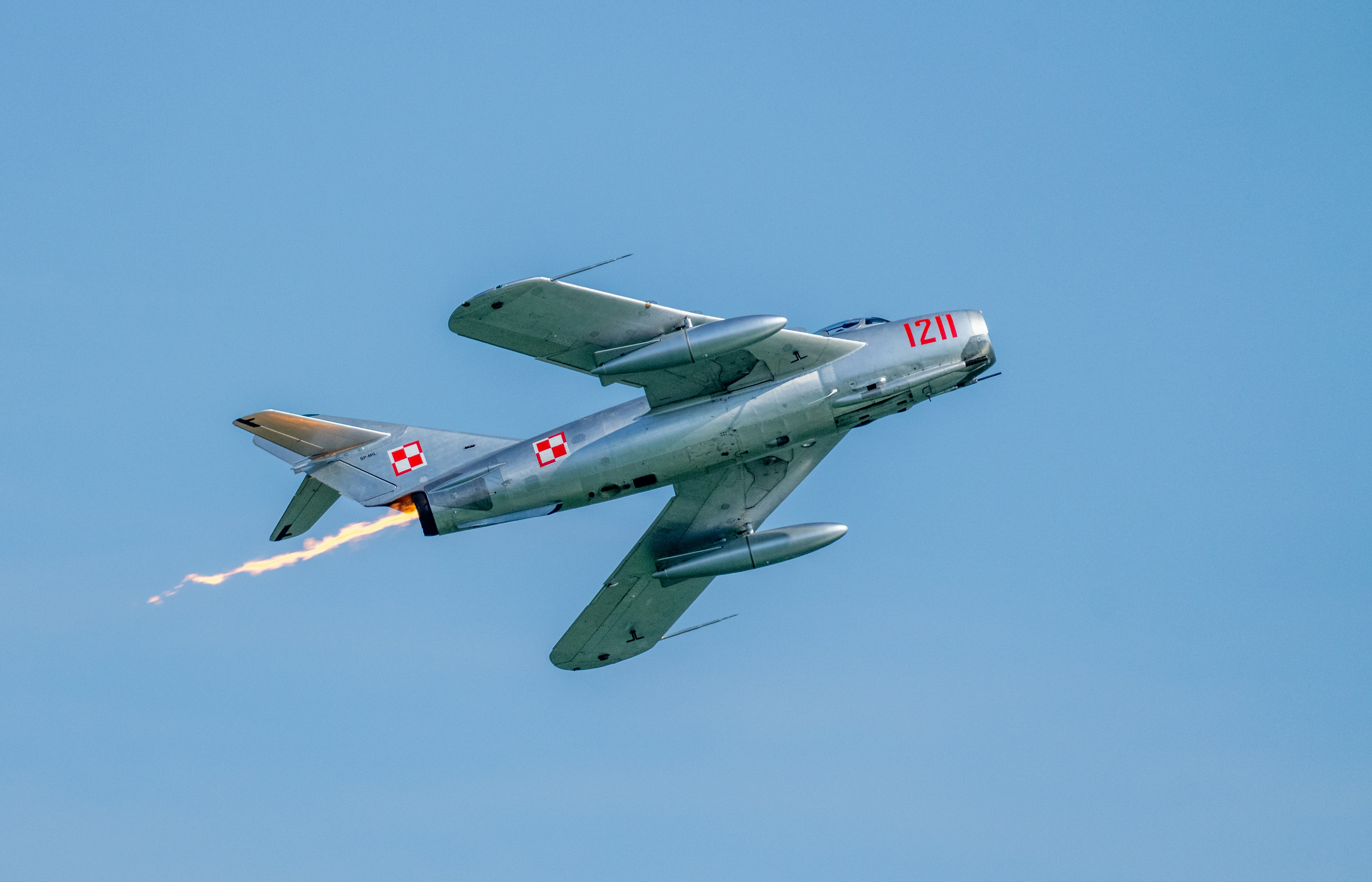 A silver jet fighter with red markings flying against a clear blue sky