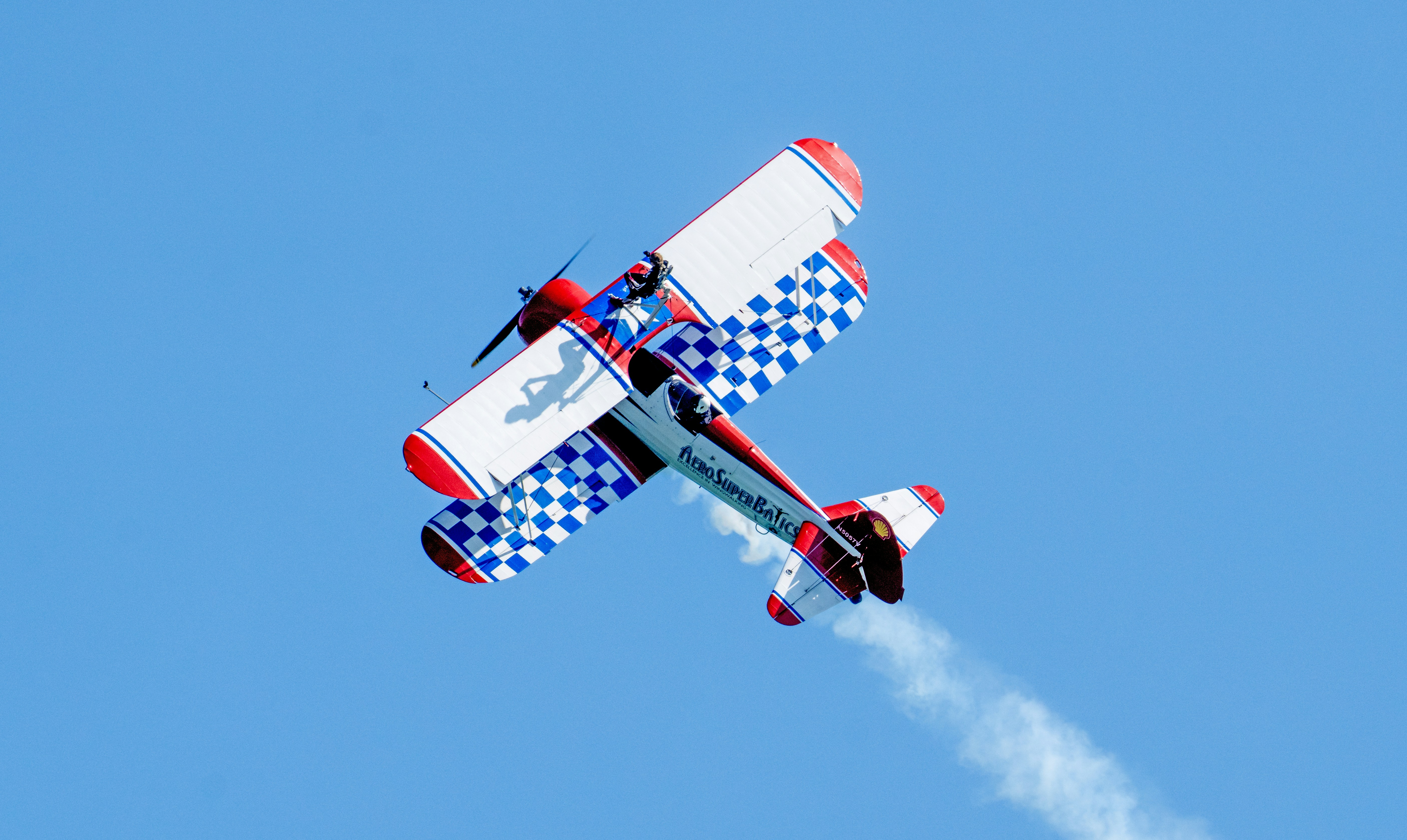A red white and blue biplane performing aerobatics against a clear blue sky