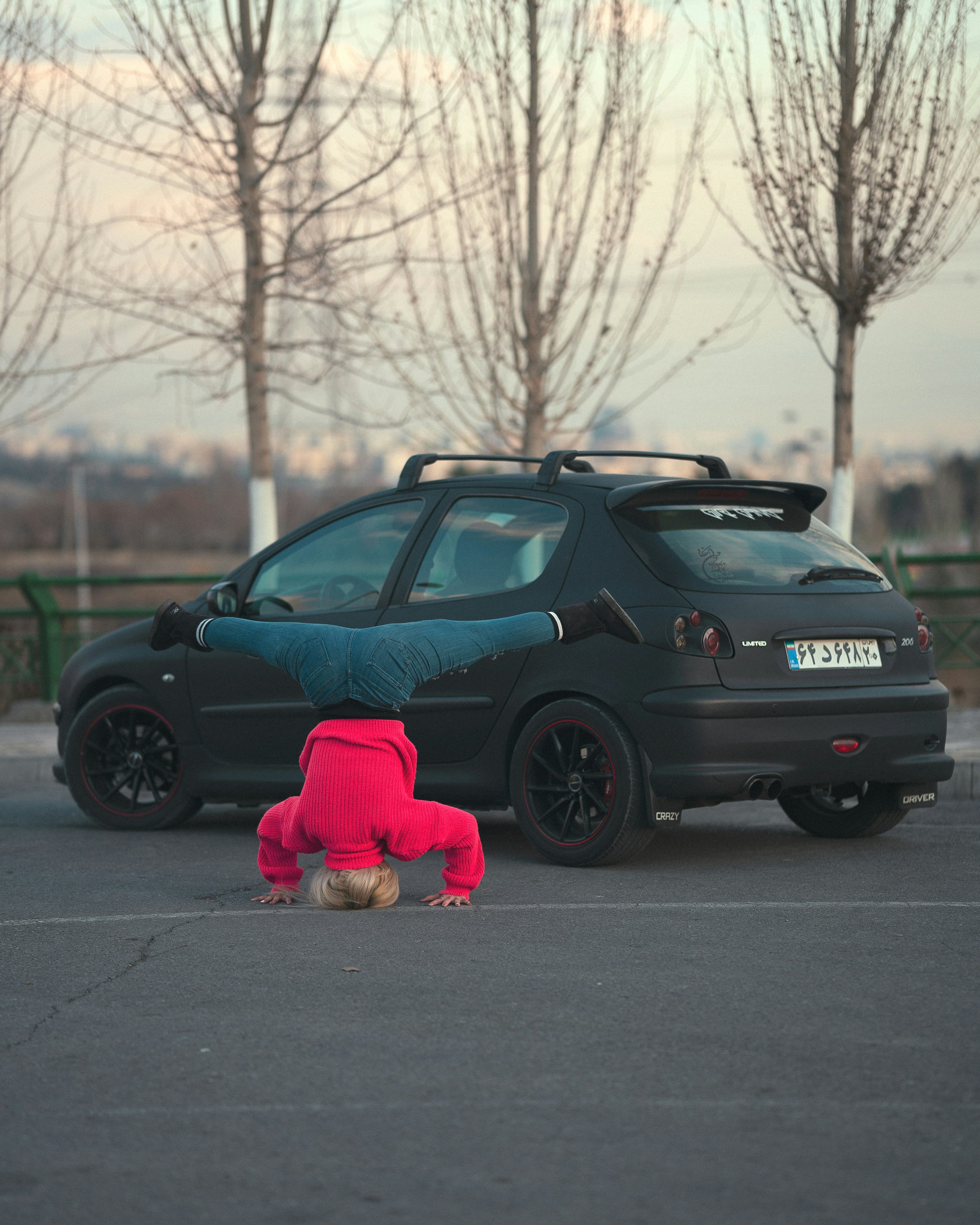 A person in a pink sweater doing a handstand in front of a black car