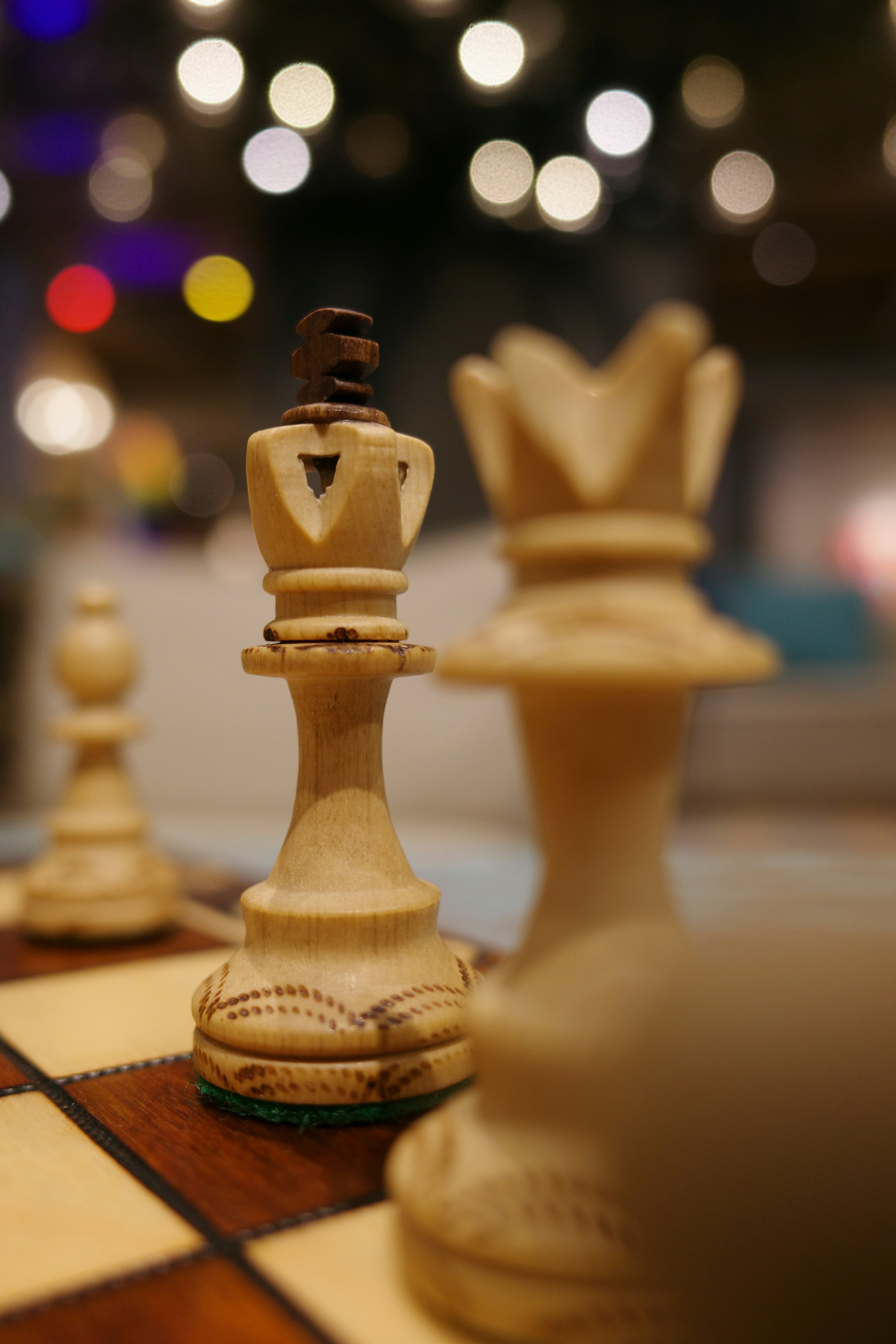 A white wooden chess king on a board with bokeh lights in the background
