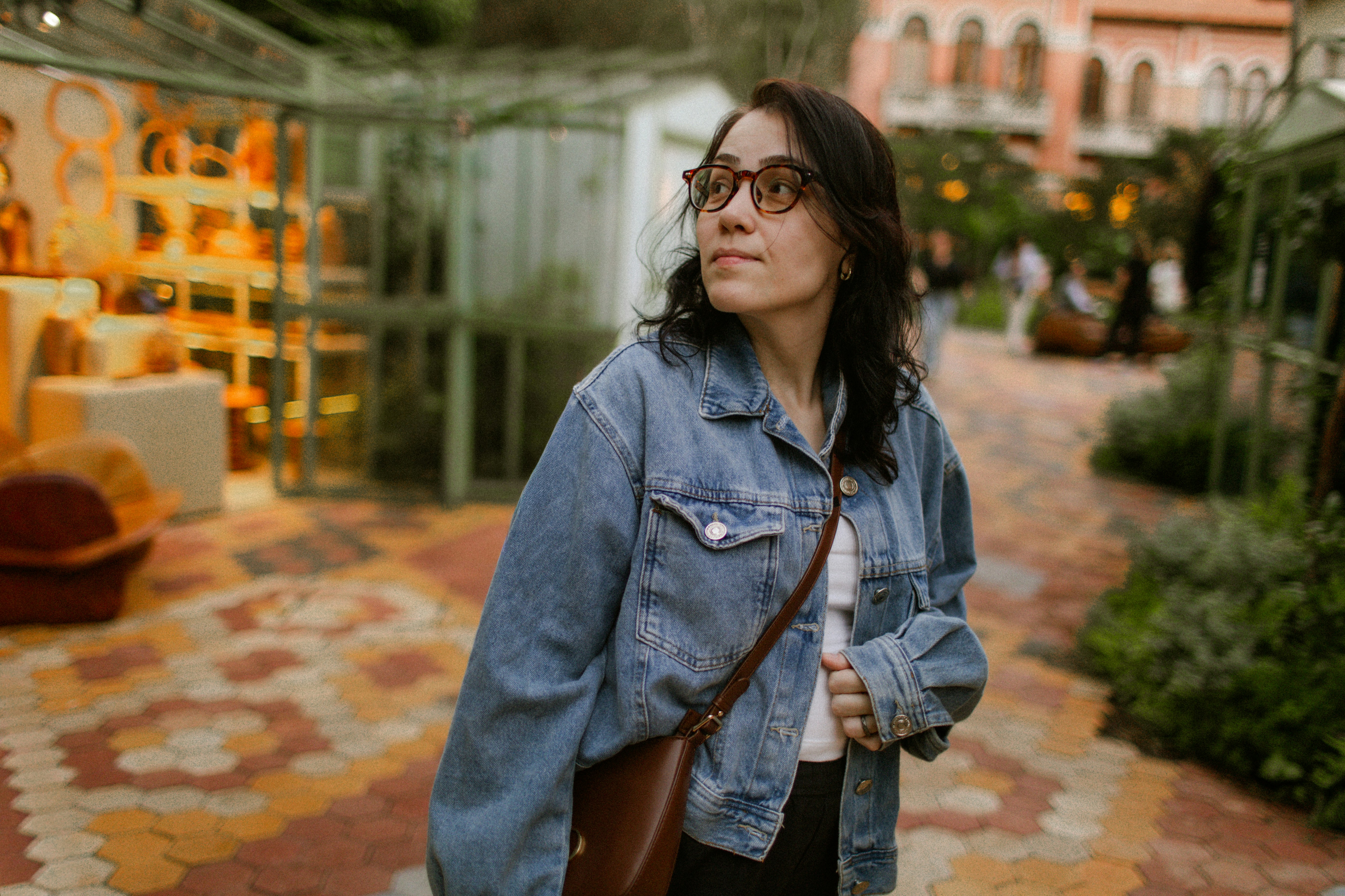 A woman in a denim jacket and glasses looking away in a garden