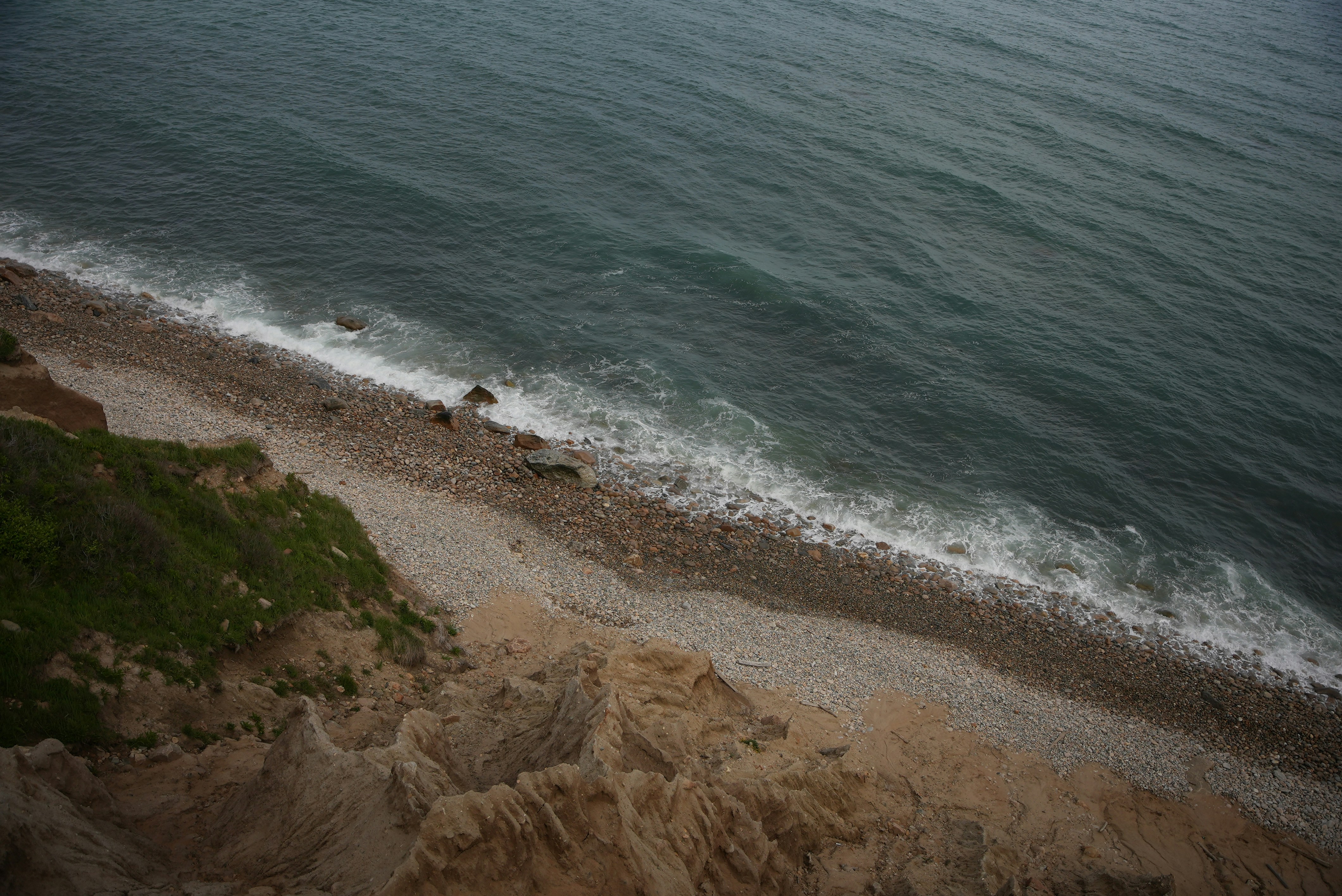 A high-angle view of a pebble beach below a grassy cliff edge