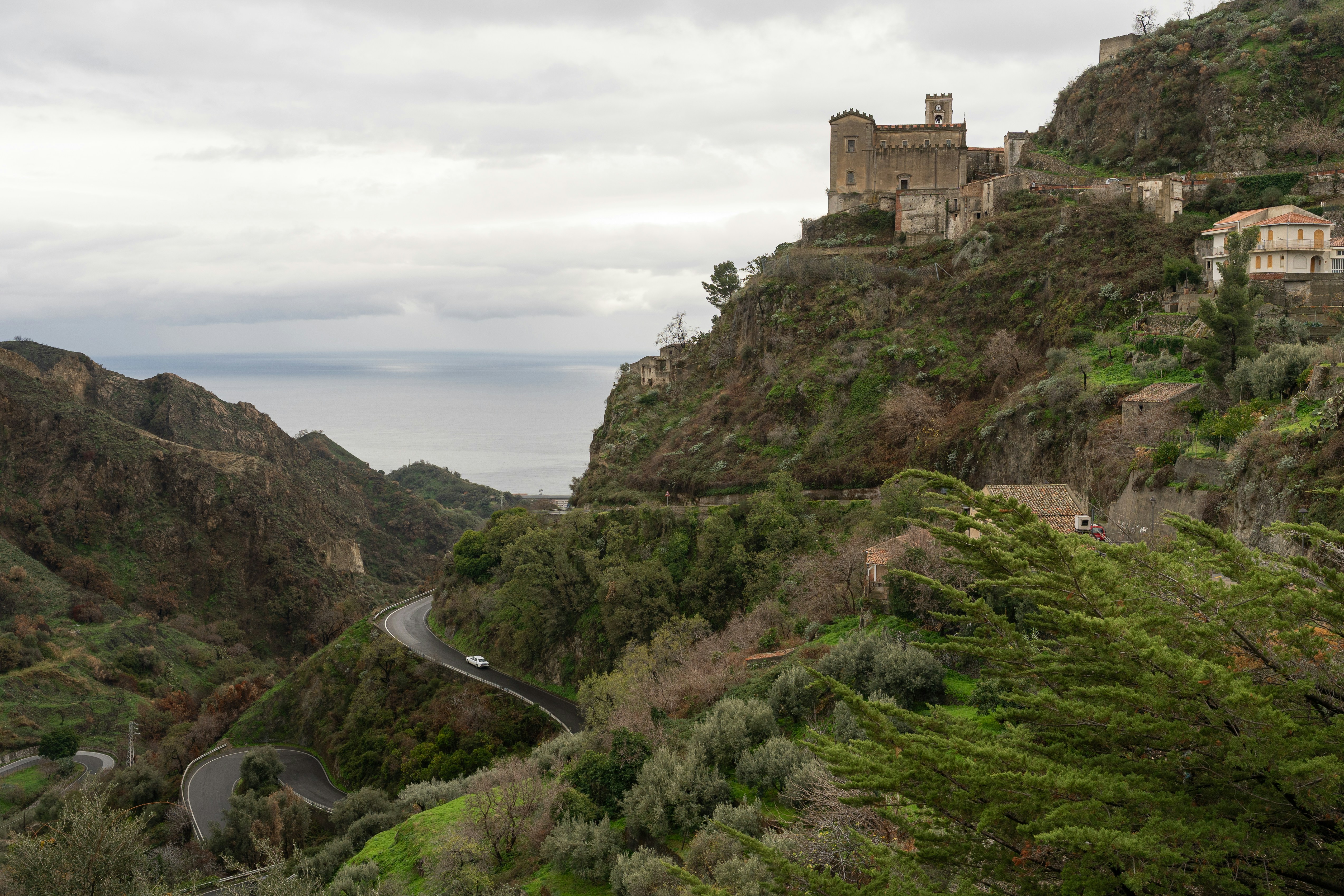 A winding road through a green valley below a hilltop castle in Sicily