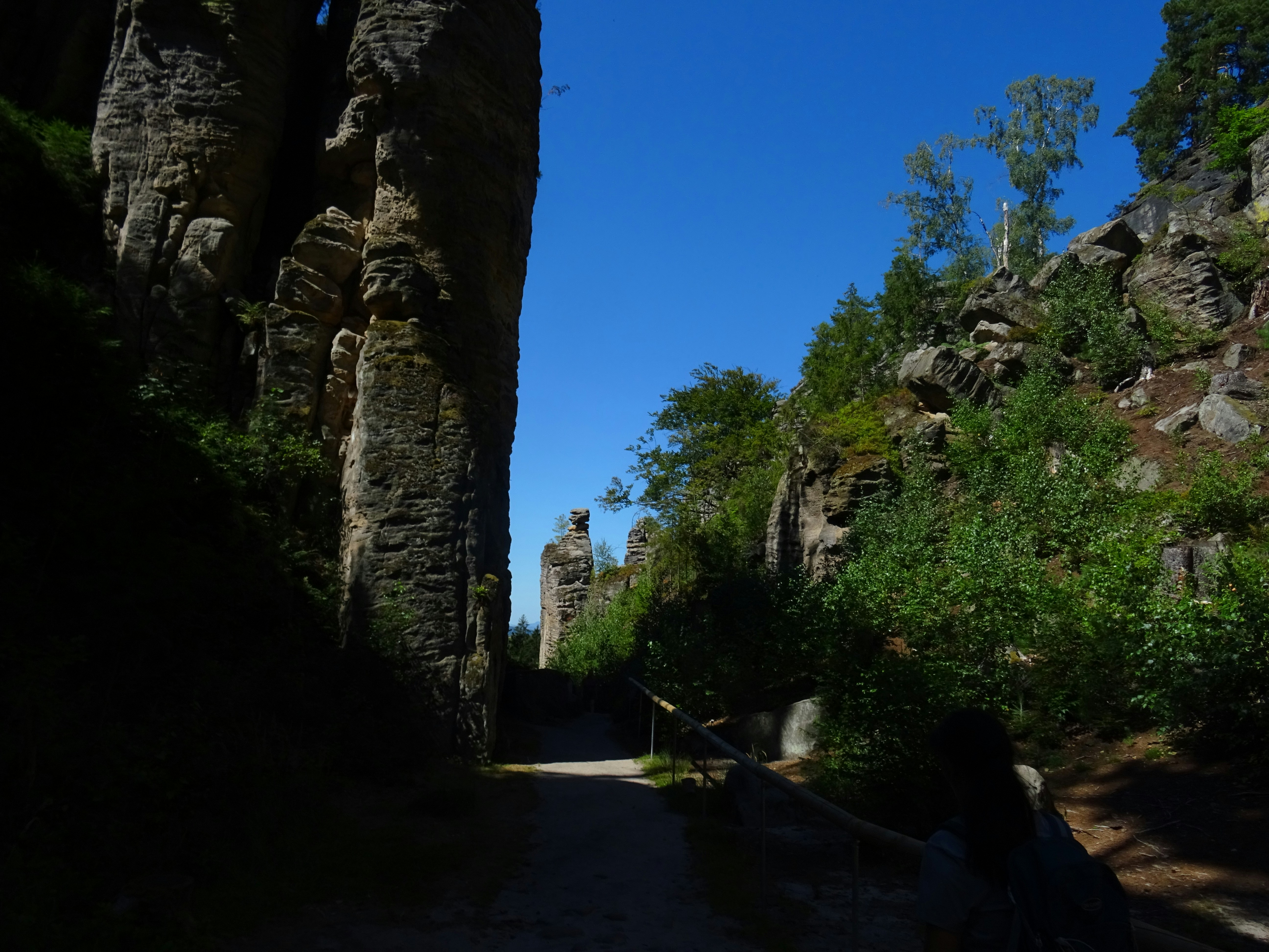 A person walking on a path between tall sandstone rock formations under blue sky
