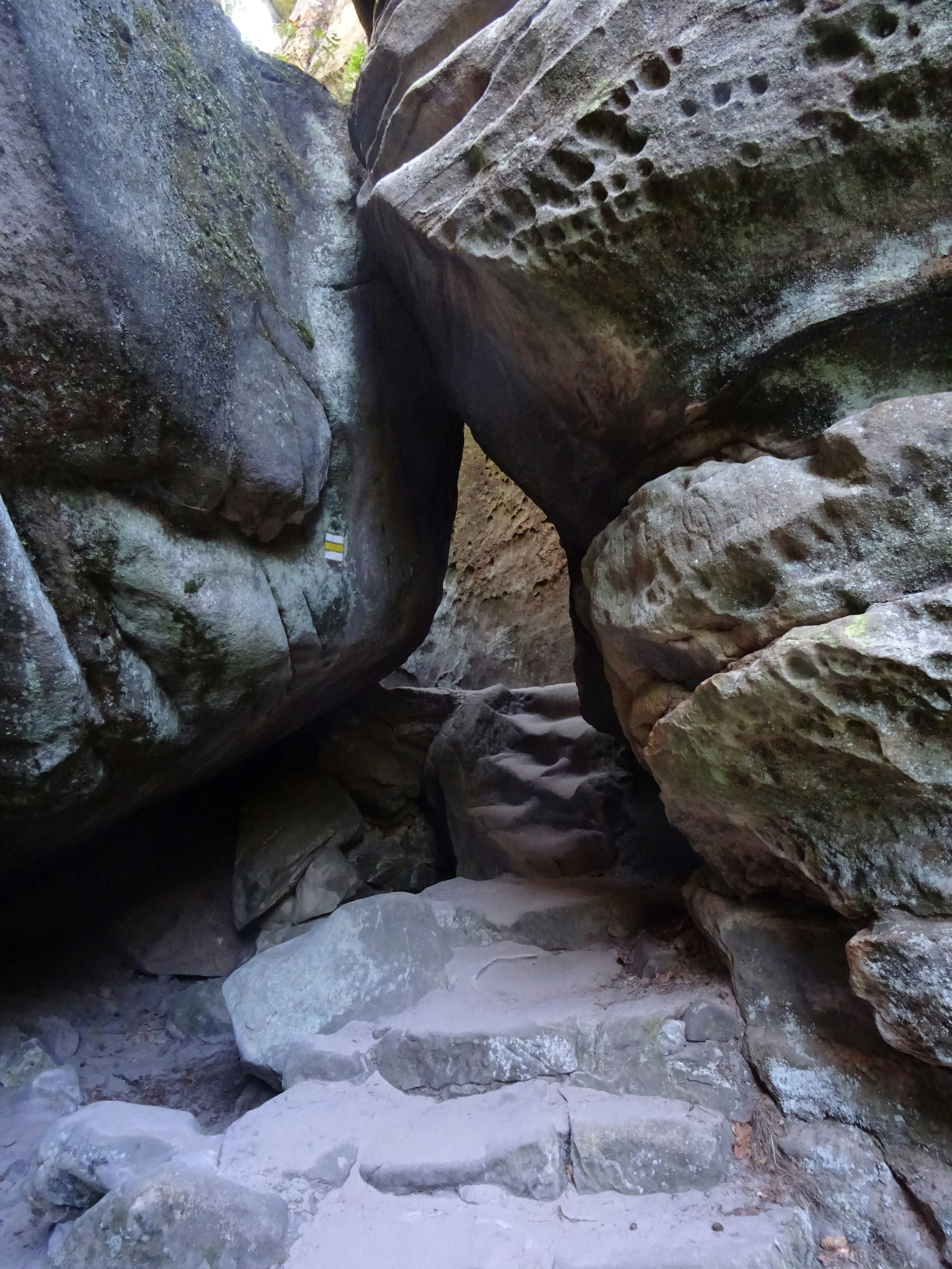 A narrow stone staircase between two large weathered sandstone boulders with a trail marker